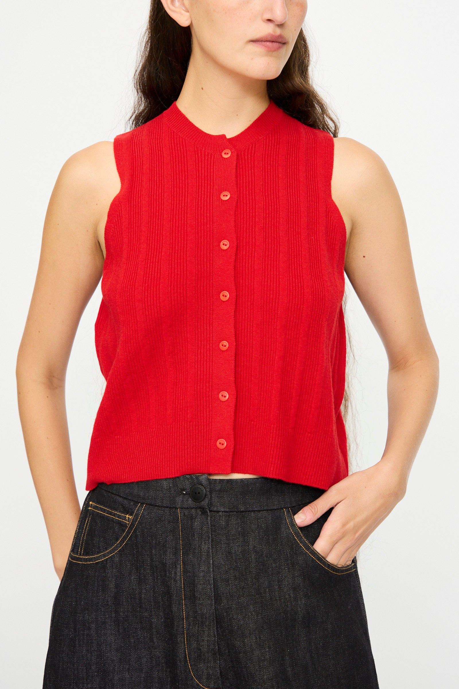 A person wearing the Cordera Merino Wool Ribbed Waistcoat in Red styled with high-waisted dark denim jeans featuring contrast stitching.