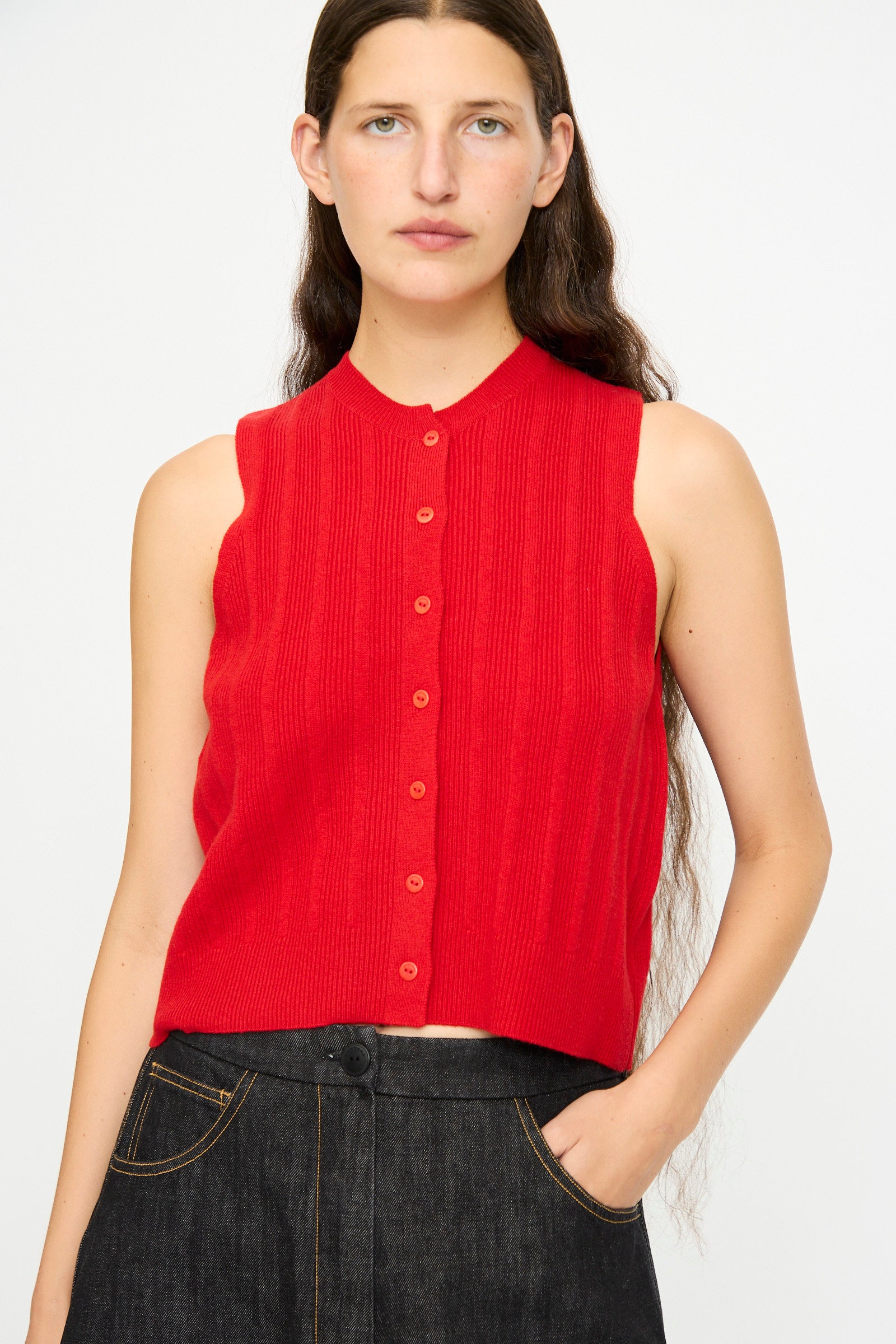 A person wearing the Cordera Merino Wool Ribbed Waistcoat in Red, paired with dark high-waisted jeans, stands against a plain light background.