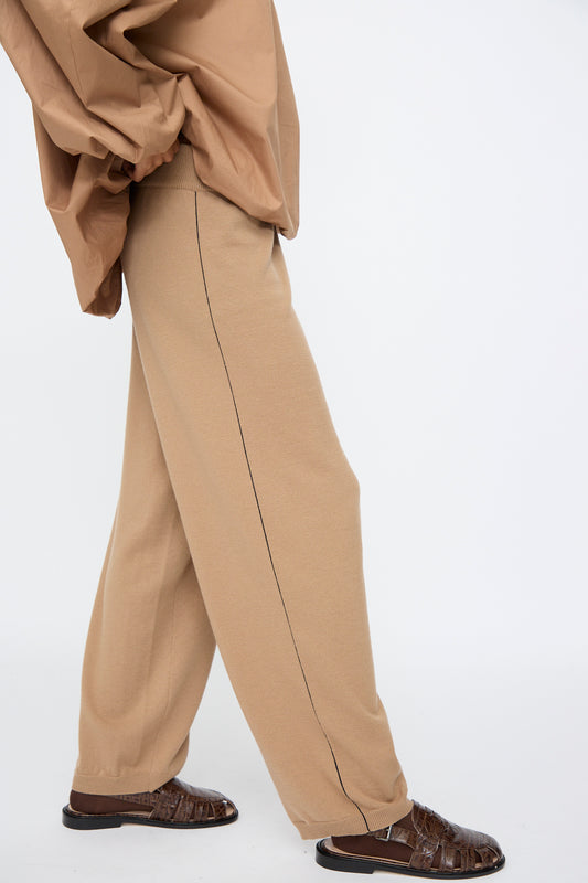 A person walks against a plain white background wearing Cordera’s Merino Wool Straight Pants in Camel—a relaxed, oversized fit—paired with a matching top and dark brown woven sandals.
