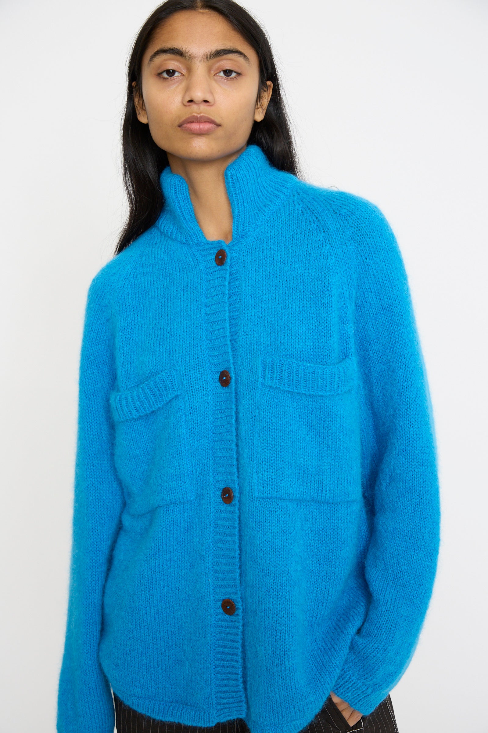 A person wearing a Cordera Mohair and Baby Alpaca Polo Jacket in Cerúleo, featuring large pockets, stands against a plain background.