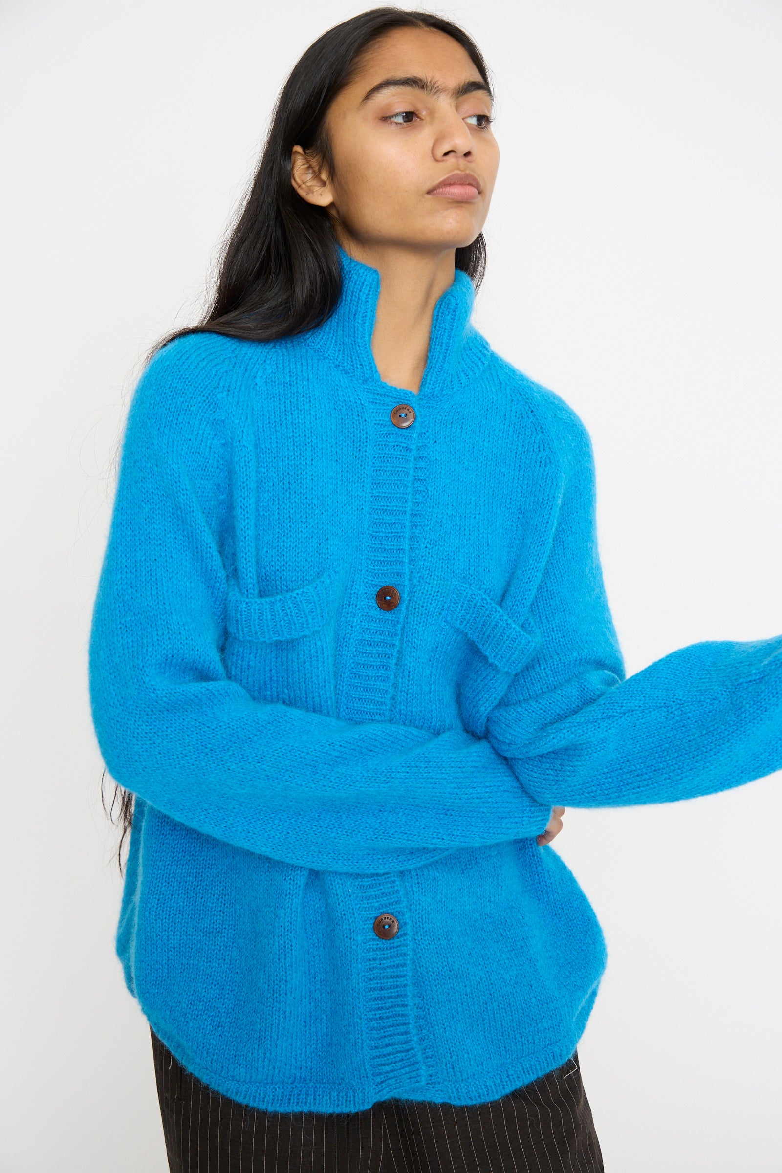 A person wearing Cordera's Mohair and Baby Alpaca Polo Jacket in Cerúleo and striped black pants stands against a plain white background.