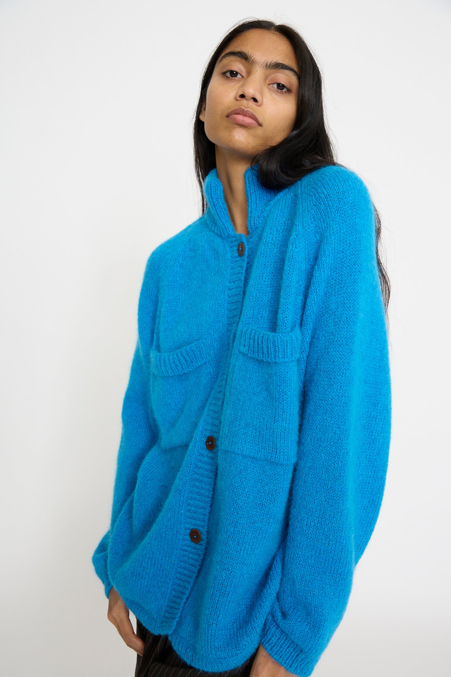 A person stands against a plain white background wearing the Cordera Mohair and Baby Alpaca Polo Jacket in Cerúleo, which is bright blue, crafted from a soft mohair blend and features two front pockets.