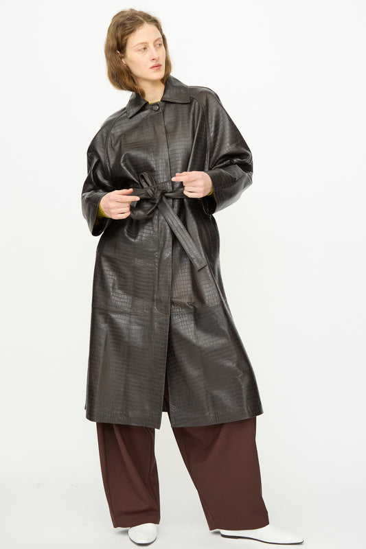 A person wears the Cordera Nappa Long Coat in Crocodile, styled with wide brown pants and white shoes, standing against a plain white background.