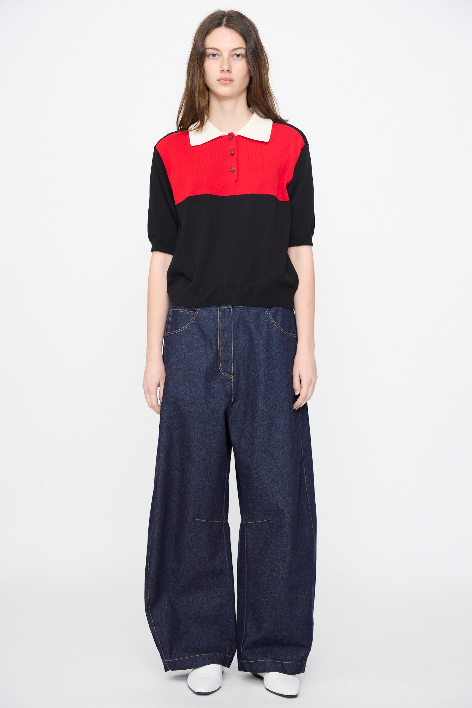 A person faces forward in a Cordera Cotton Polo in Colorblock, paired with wide-leg dark jeans and white shoes, set against a plain white background.