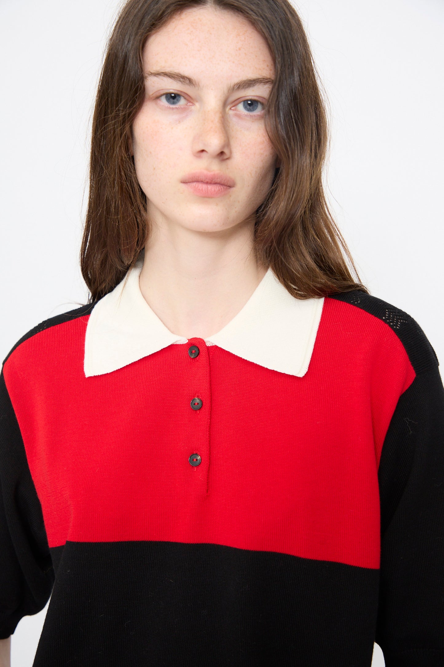 A person with long brown hair wears the Cordera Cotton Polo in Colorblock, featuring a cream collar, and looks directly at the camera against a plain background.