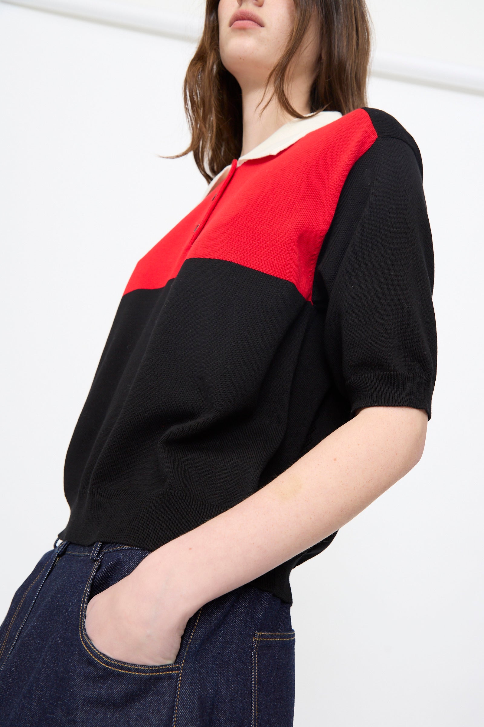 A person wears the Cordera Cotton Polo in Colorblock (red and black), styled with dark blue jeans, standing against a plain white background.