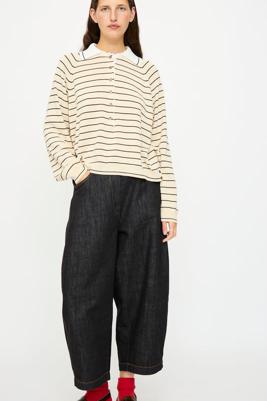A person wears the Cordera Organic Cotton Polo in Striped—cream and black, oversized fit—with wide-leg dark denim pants and red socks, standing against a plain white background.