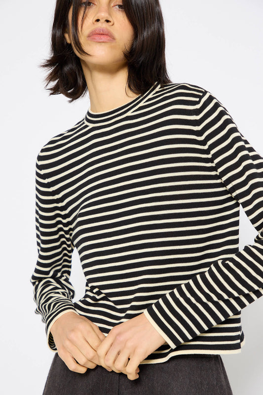 Person with dark shoulder-length hair wearing Cordera's Organic Cotton T-Shirt in Striped and dark pants, against a plain background.