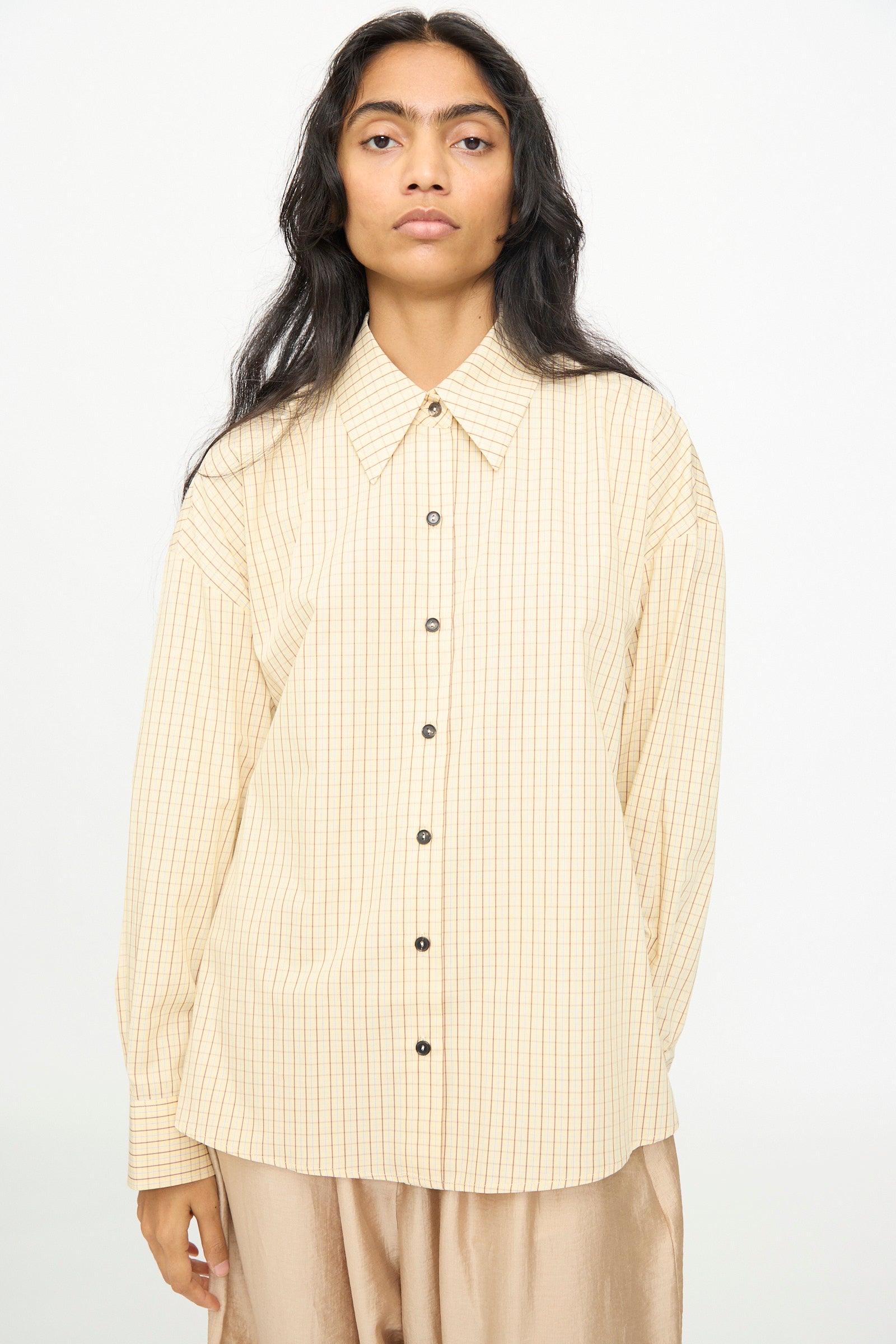 A person stands against a plain background wearing Cordera’s Oversized Shirt in Checked, featuring a wide Italian collar and long sleeves.
