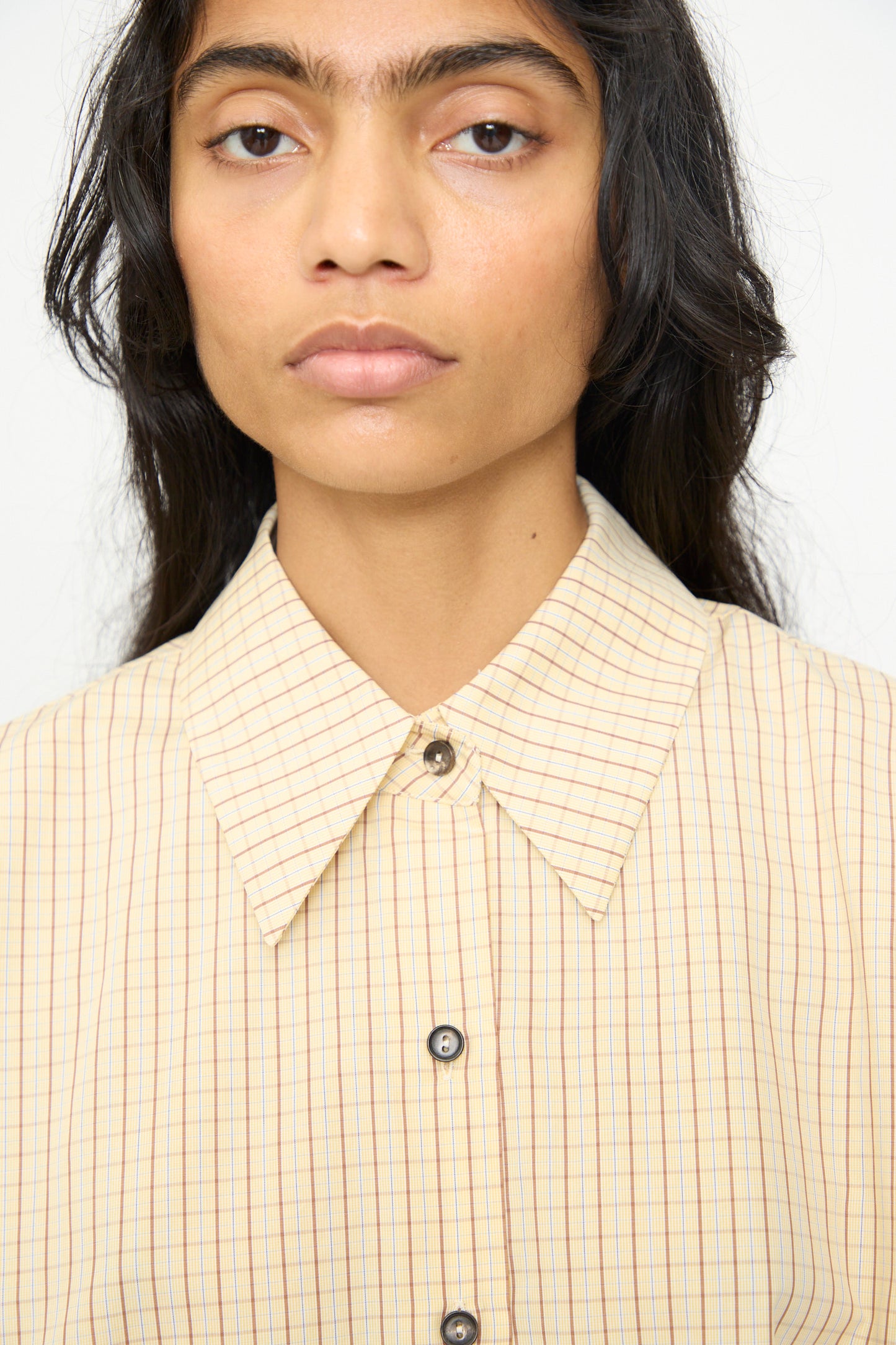 A person with long dark hair wears the Cordera Oversized Shirt in Checked, featuring an Italian collar, shown from the shoulders up against a plain background.