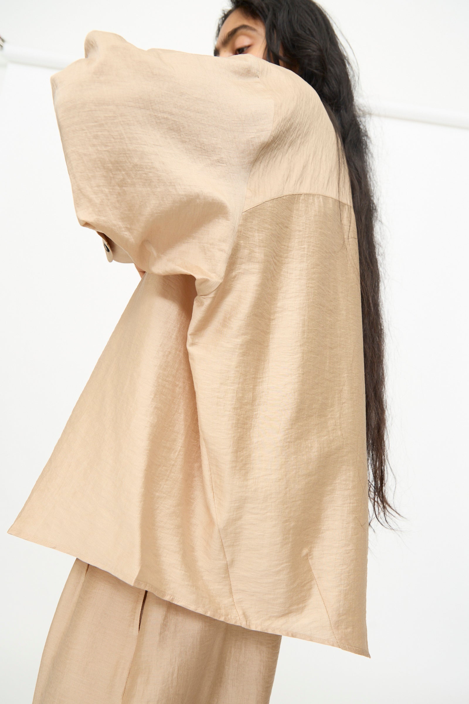 A person wearing the Cordera Oversized Shirt in Beige, photographed from the side against a plain white background, with their head partially out of frame.