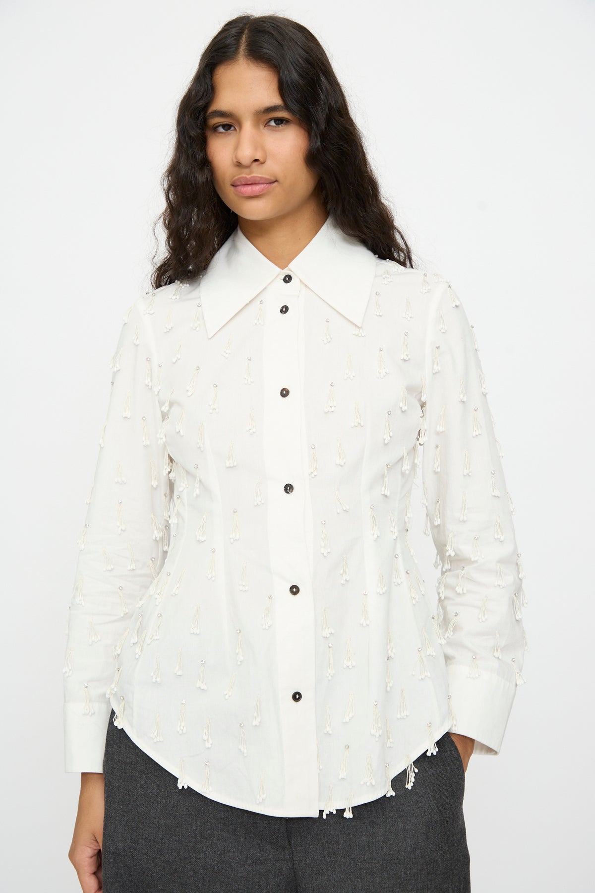 A person wearing the Cordera Petalos Shirt in White, a fitted long-sleeved button-up with a pointed collar and small dangling bead embellishments.