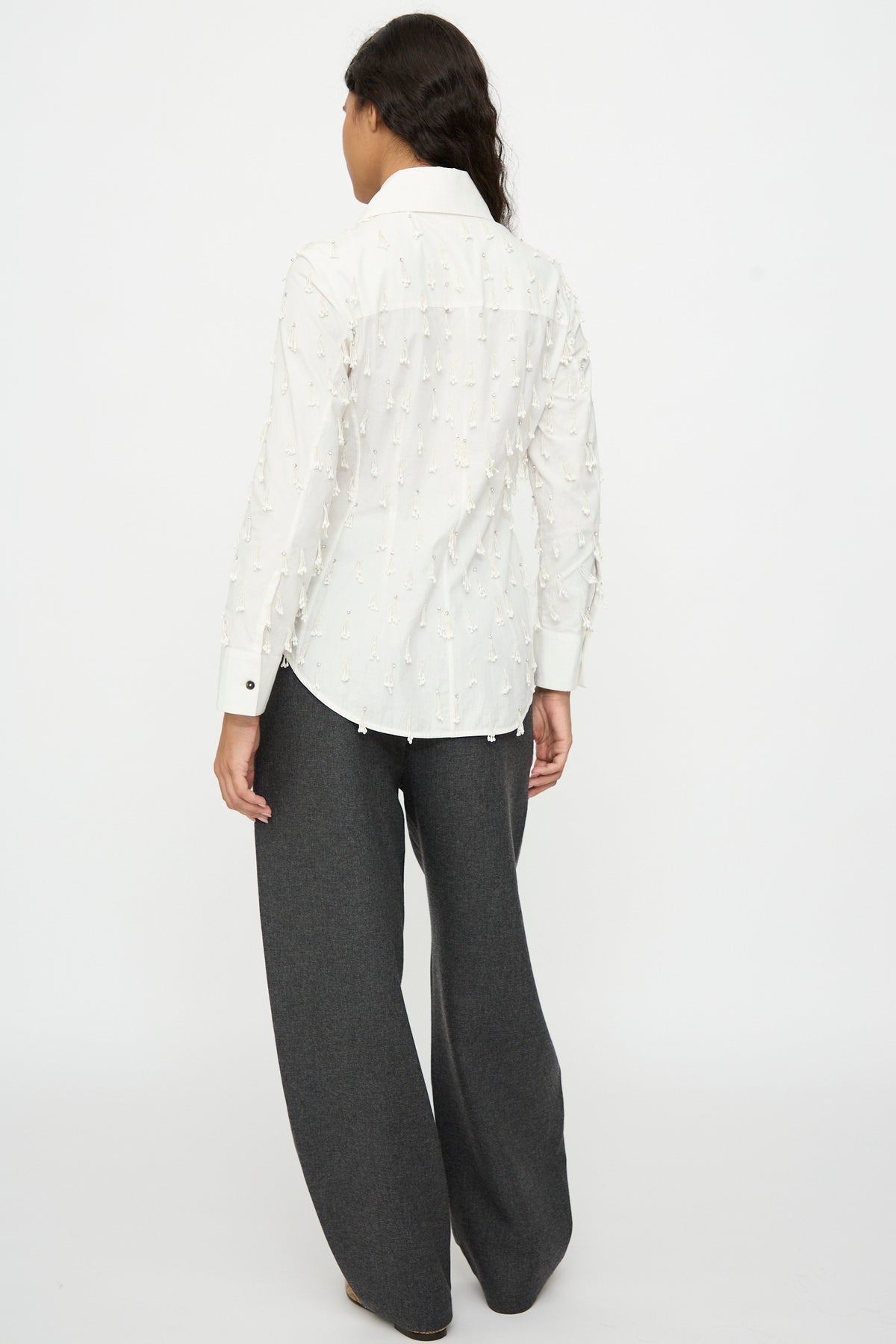 Cordera Petalos Shirt in white, a fitted long-sleeved button-down with small fringe embellishments, worn with dark gray wide-leg trousers.