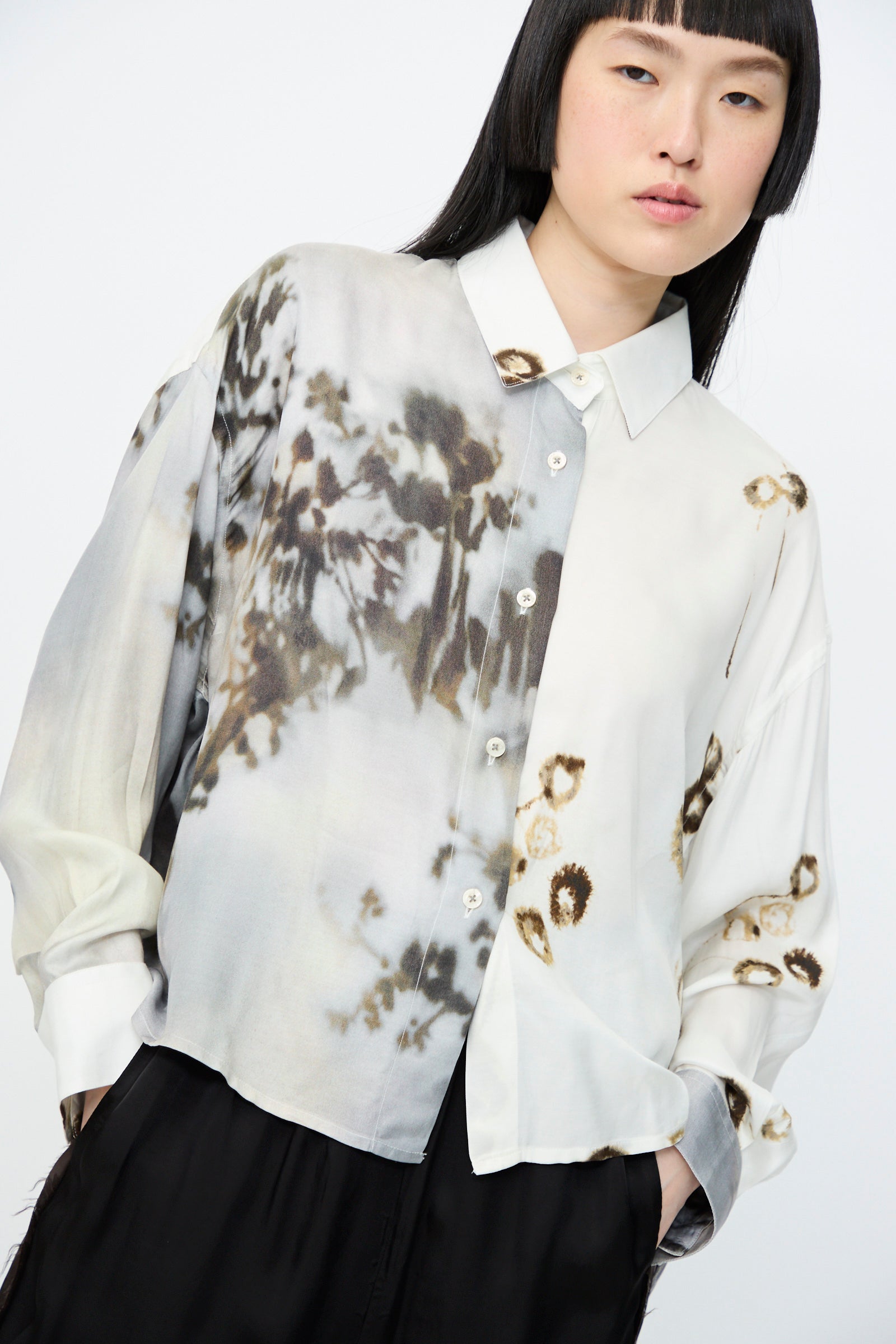 A person wearing Cordera's Printed Classic Shirt in Bicolor, styled in an oversized fit, paired with black pants, stands against a plain background.