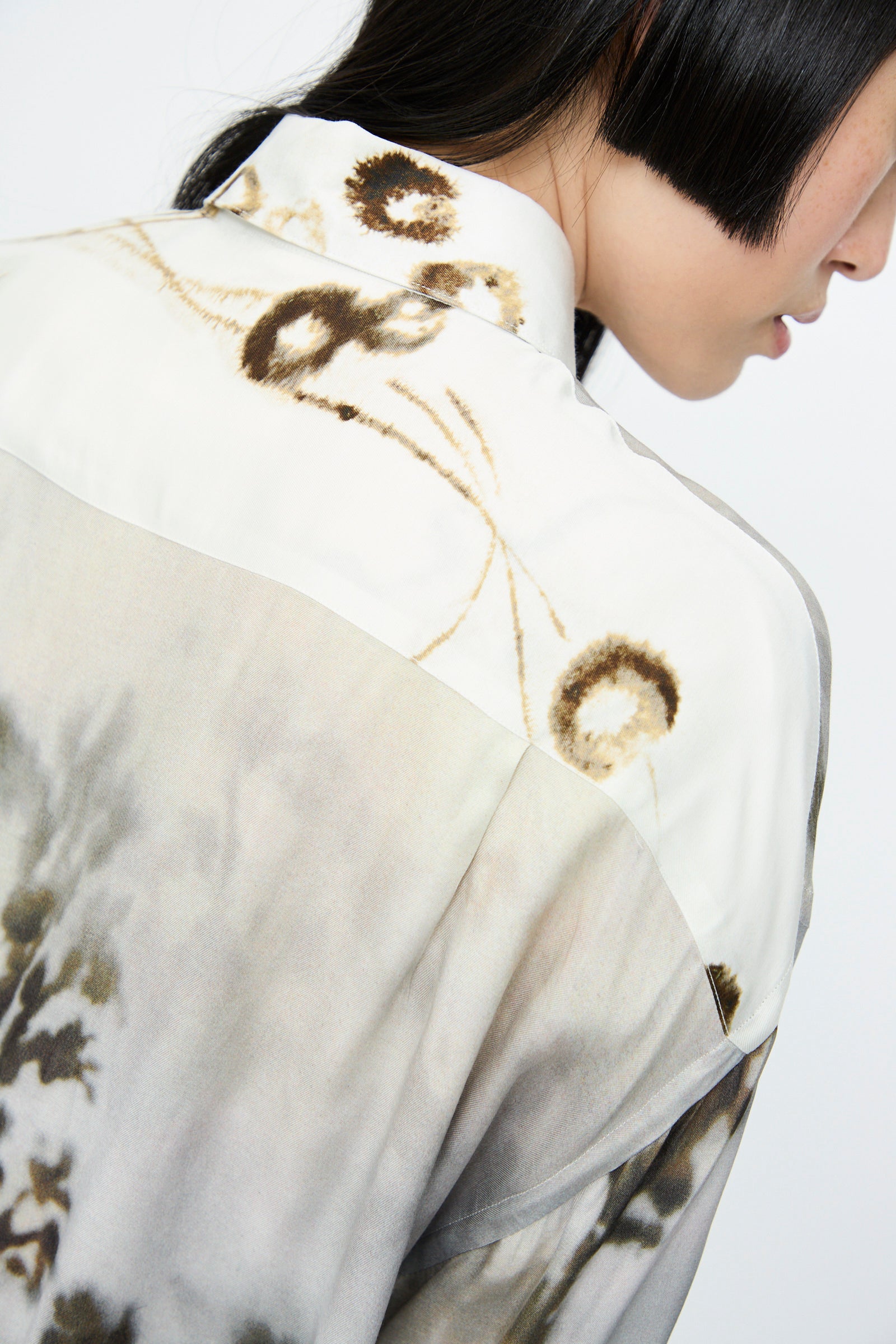 Close-up of a person with short black hair wearing Cordera's Printed Classic Shirt in Bicolor, boasting a nature-inspired pattern with abstract brown and beige designs on a light background, made from soft printed viscose.