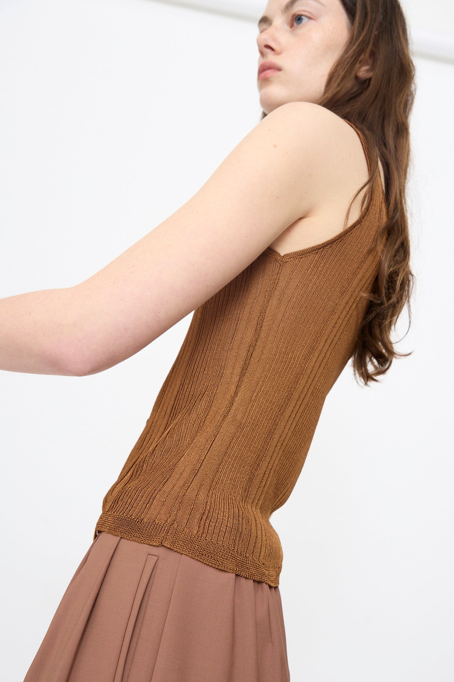 A person wears the Cordera Ribbed Tank Top in Tobacco and a brown pleated skirt, standing against a plain white background.
