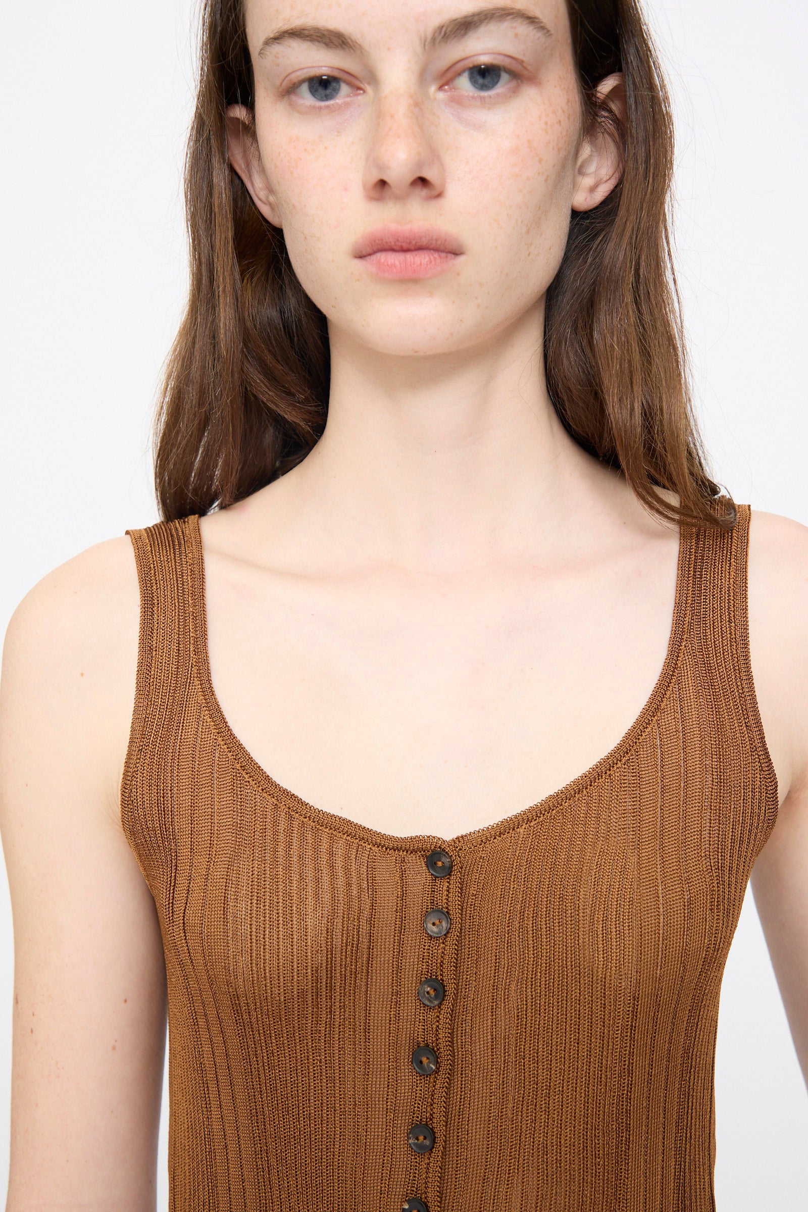 A woman with long brown hair wears the Cordera Ribbed Tank Top in Tobacco, featuring front buttons, while standing against a plain white background.