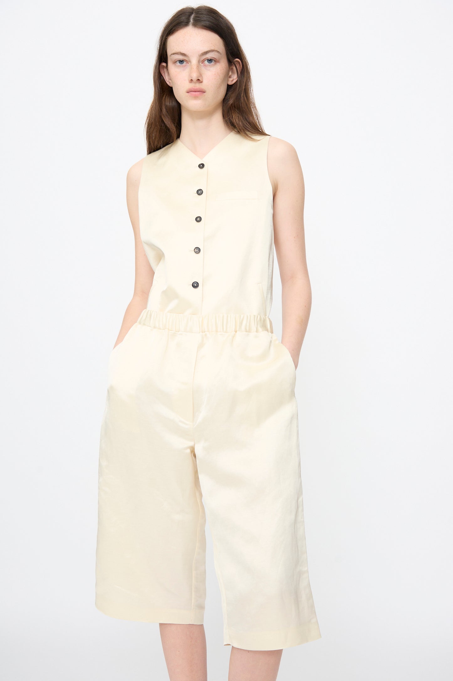 Model wears Cordera's Satin Capri Pants in Off White, featuring a relaxed fit and wide legs, with hands in pockets, standing against a plain white background.