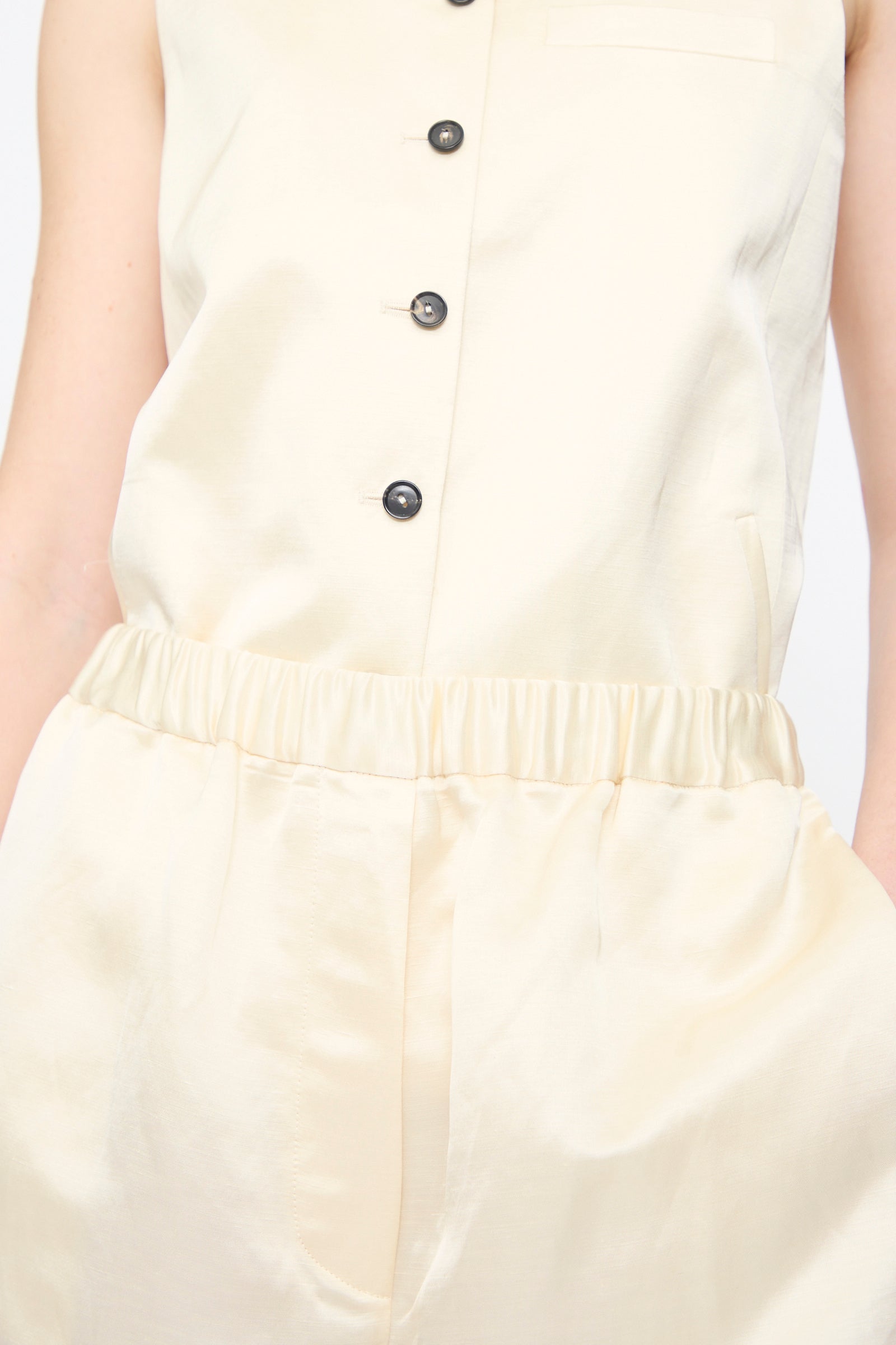 Person wearing Cordera's Satin Capri Pants in Off White, paired with a sleeveless cream button-up top; shown from shoulders to upper thighs.