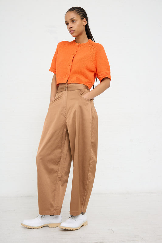 Woman in orange top and high-rise Cordera relaxed fit pants in Camel against a white background.