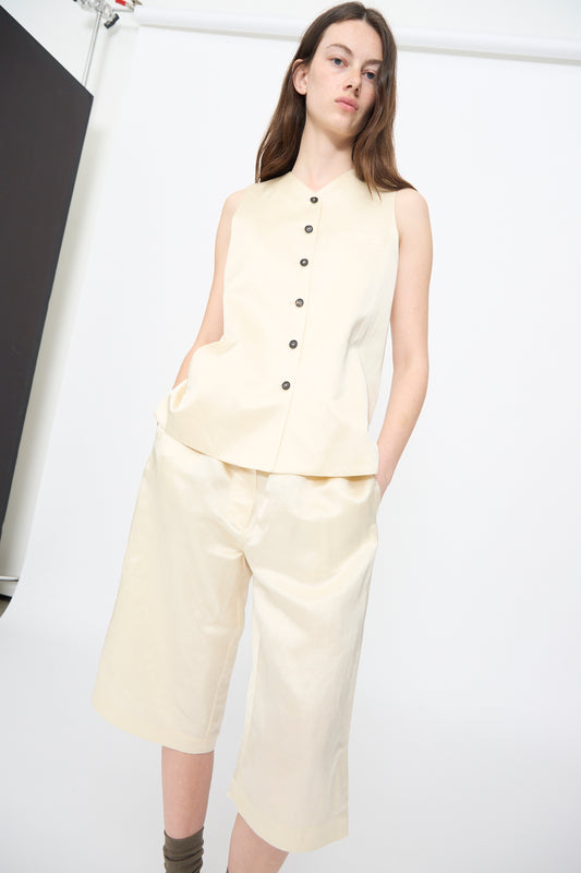 Someone models the Cordera Satin Tailored Vest in Marfil paired with matching knee-length shorts, standing with hands in pockets against a plain, light background.