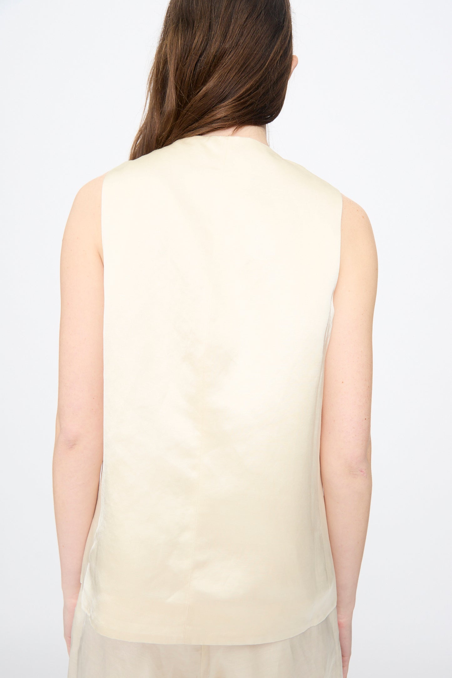 A person with long brown hair is shown from the back, wearing Cordera’s Satin Tailored Vest in Marfil against a plain background.