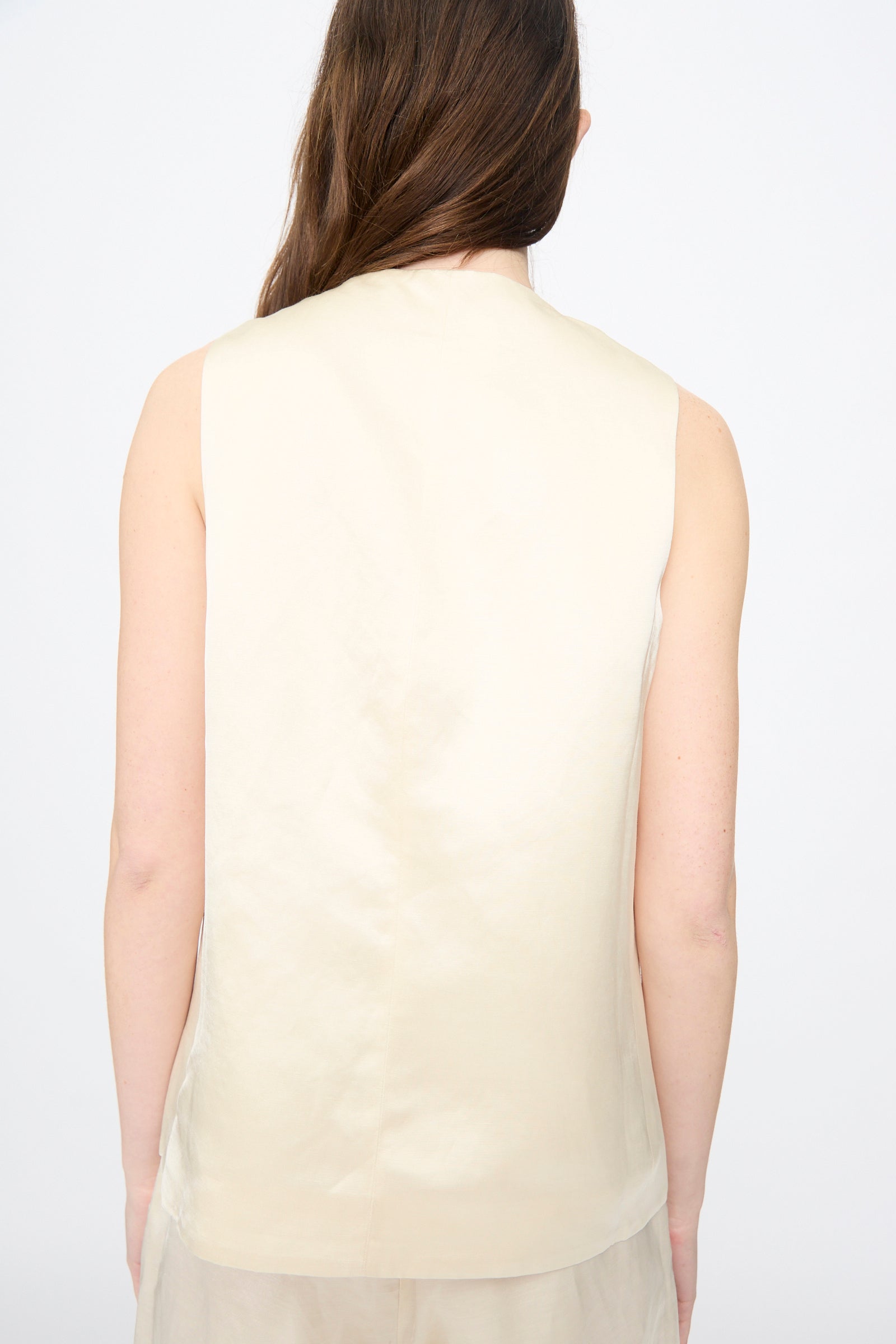A person with long brown hair is shown from the back, wearing Cordera’s Satin Tailored Vest in Marfil against a plain background.
