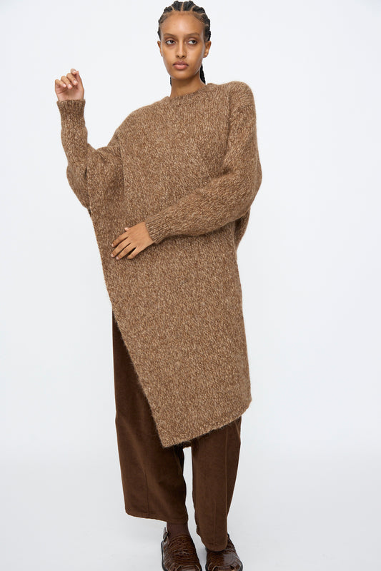 A person wearing an oversized brown knit sweater, wide-leg pants, dark shoes, and the Cordera Scarf in Brown Melange stands against a plain white background.