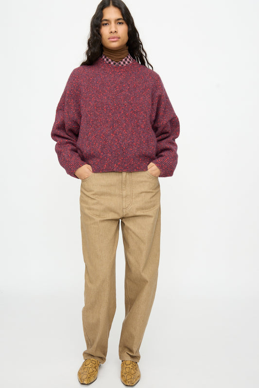A person wearing a maroon Speckled Crewneck Sweater in Beaujolais over a collared shirt, paired with tan trousers and snakeskin-patterned shoes.