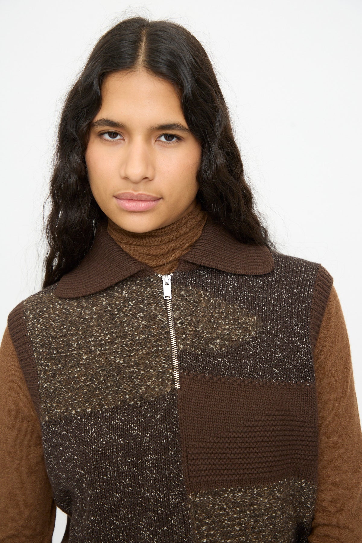 A person wearing a Cordera Speckled Waistcoat in Brown, a patchwork wool blend knit waistcoat, over a brown turtleneck.
