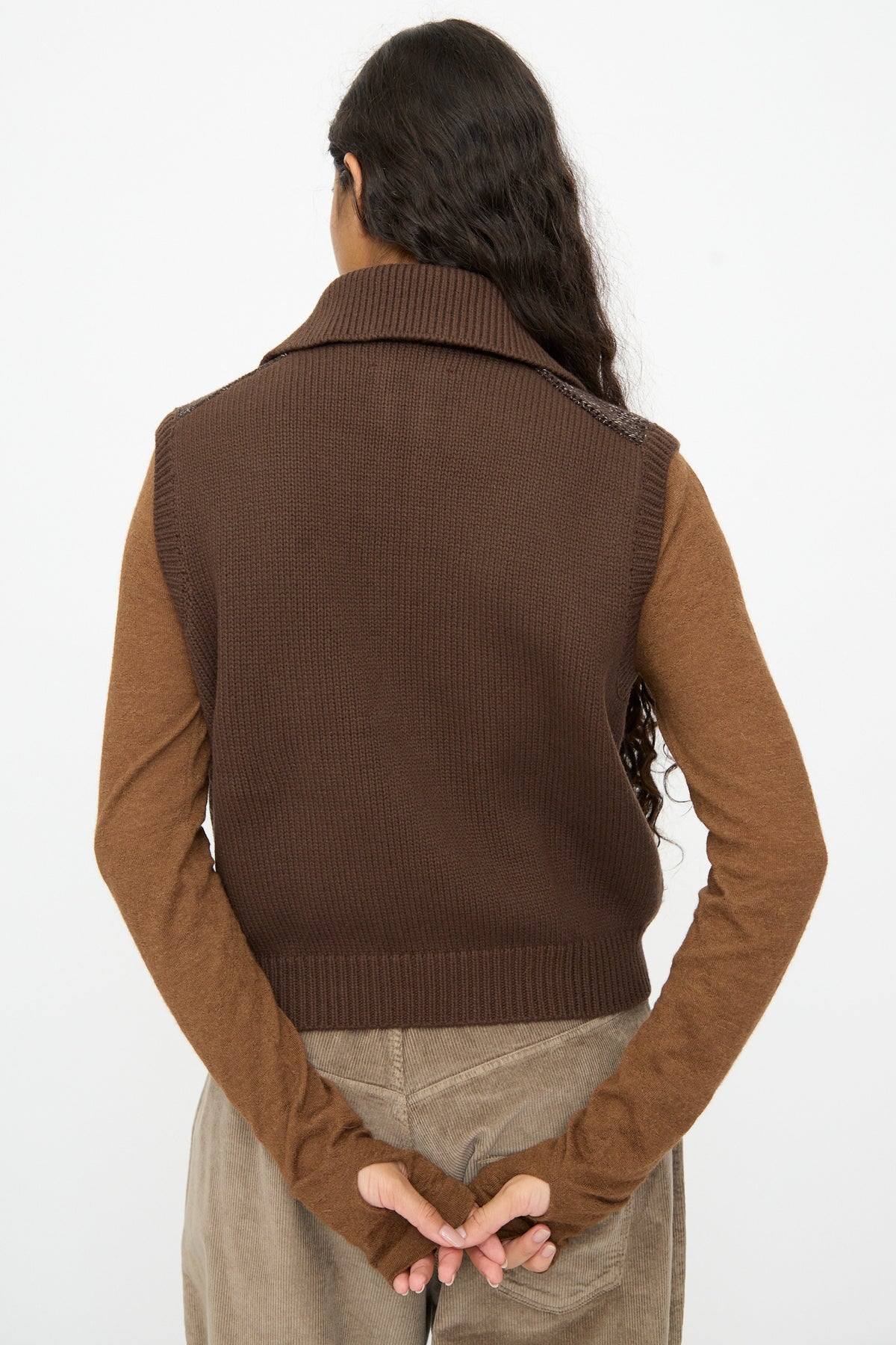 Back view of a brown patchwork Cordera Speckled Waistcoat in Brown with a polo collar, worn over a long-sleeved brown top and tan pants.