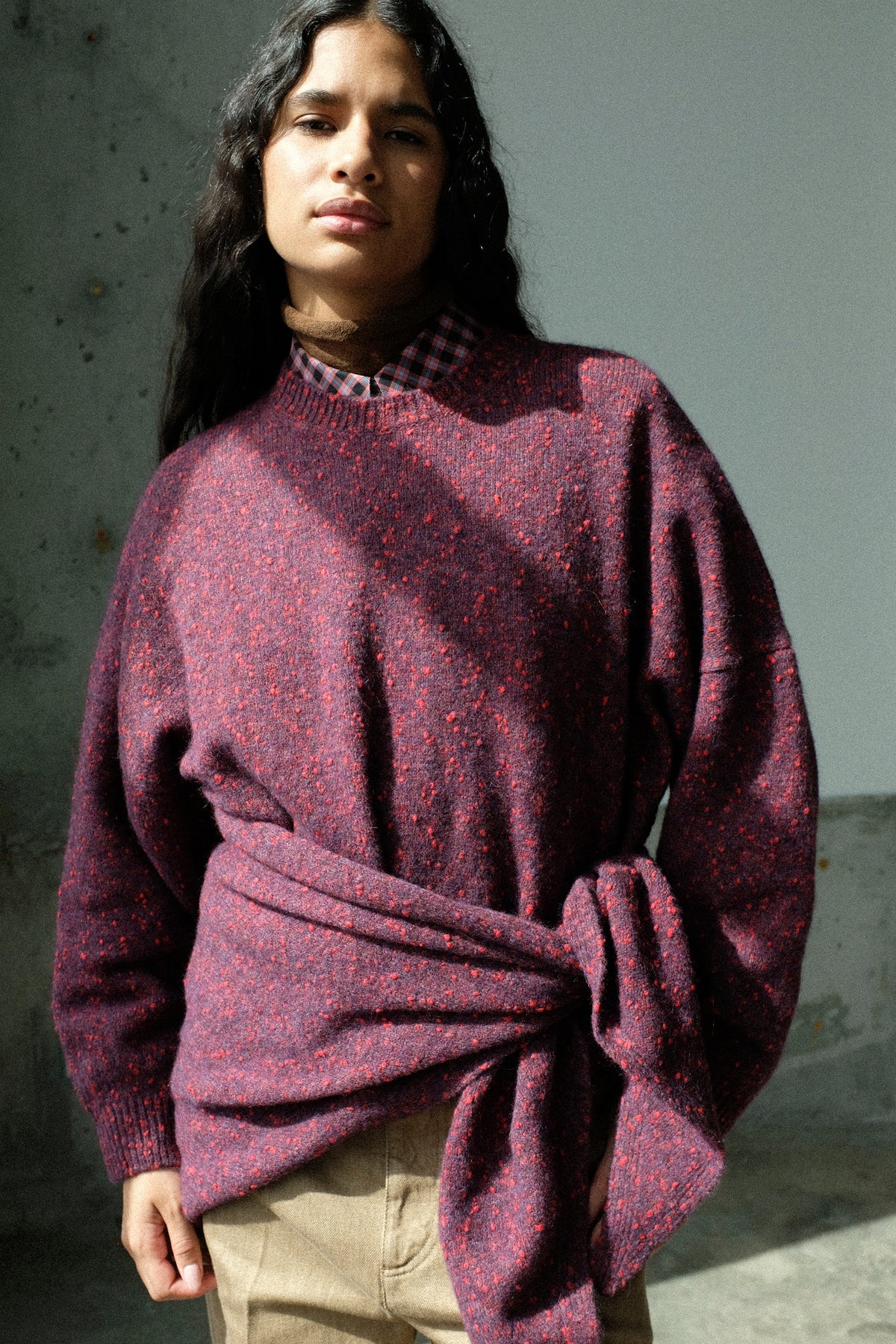 A woman in a sunlight studio wearing Cordera's Speckled Crewneck Sweater in Beaujolais, with the Maxi Bandana in Beaujolais on her waist.