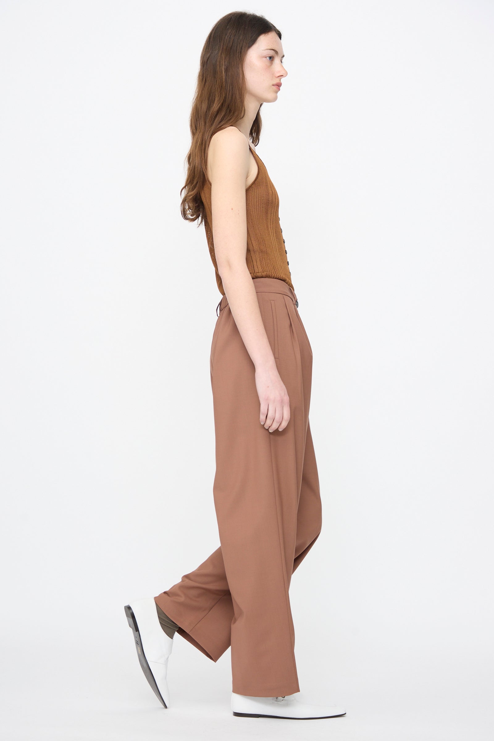 A person in profile wears Cordera’s Tailored Masculine Pant in Clove, paired with a brown sleeveless top and white shoes, set against a plain white background.