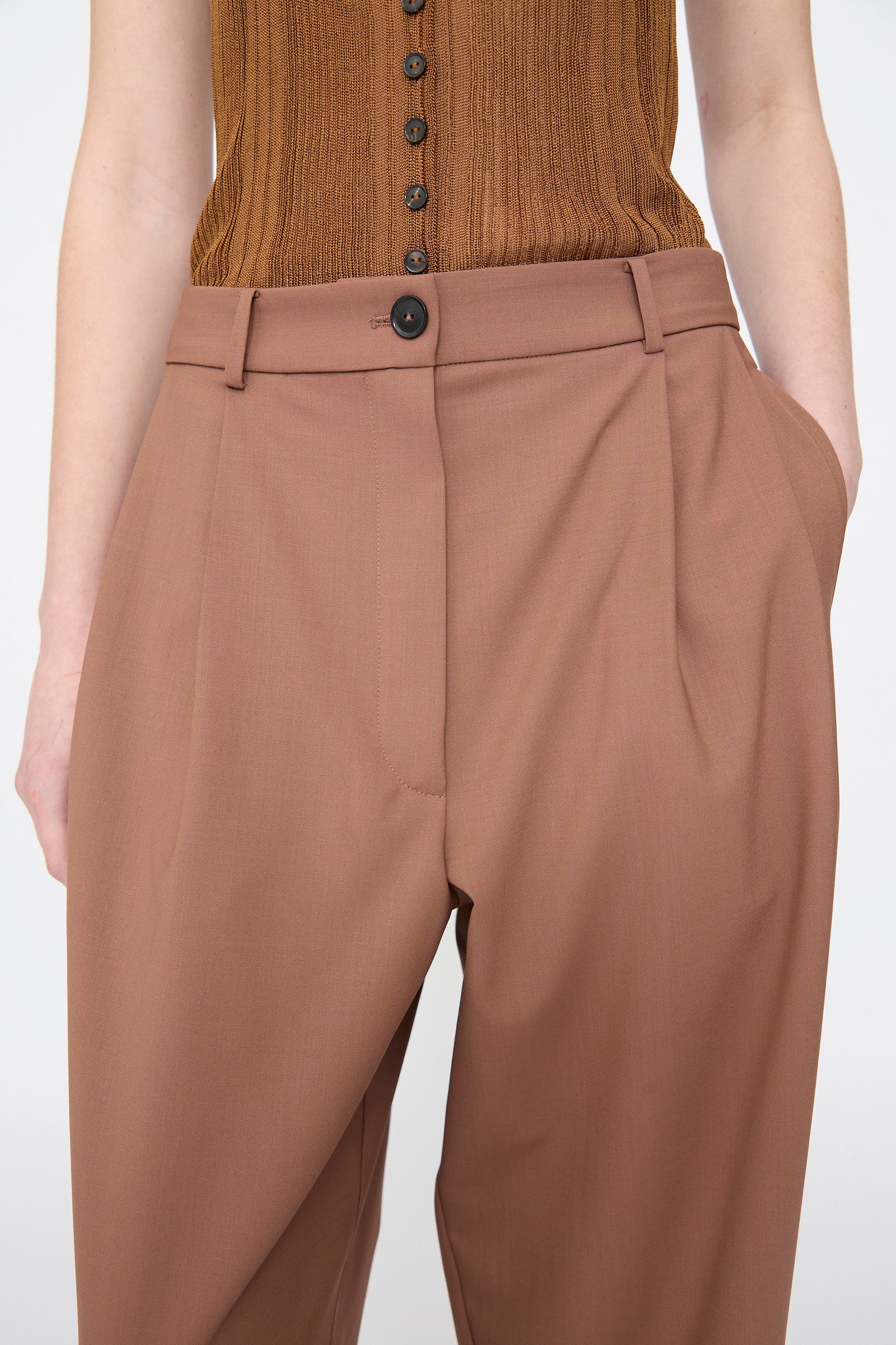 Model wears Cordera's Tailored Masculine Pant in Clove with hands in pockets, paired with a brown sleeveless buttoned top.