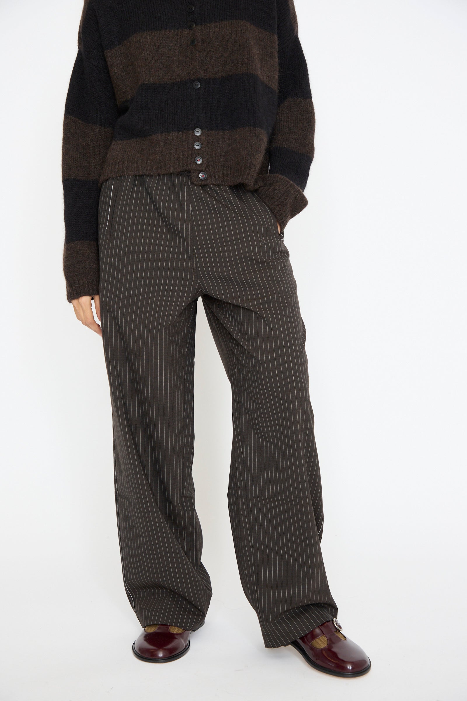 Against a white backdrop, a person wears Cordera's brown and black striped sweater with Tailoring Relaxed Pant in Shade, which has a comfortable drawstring waist. 