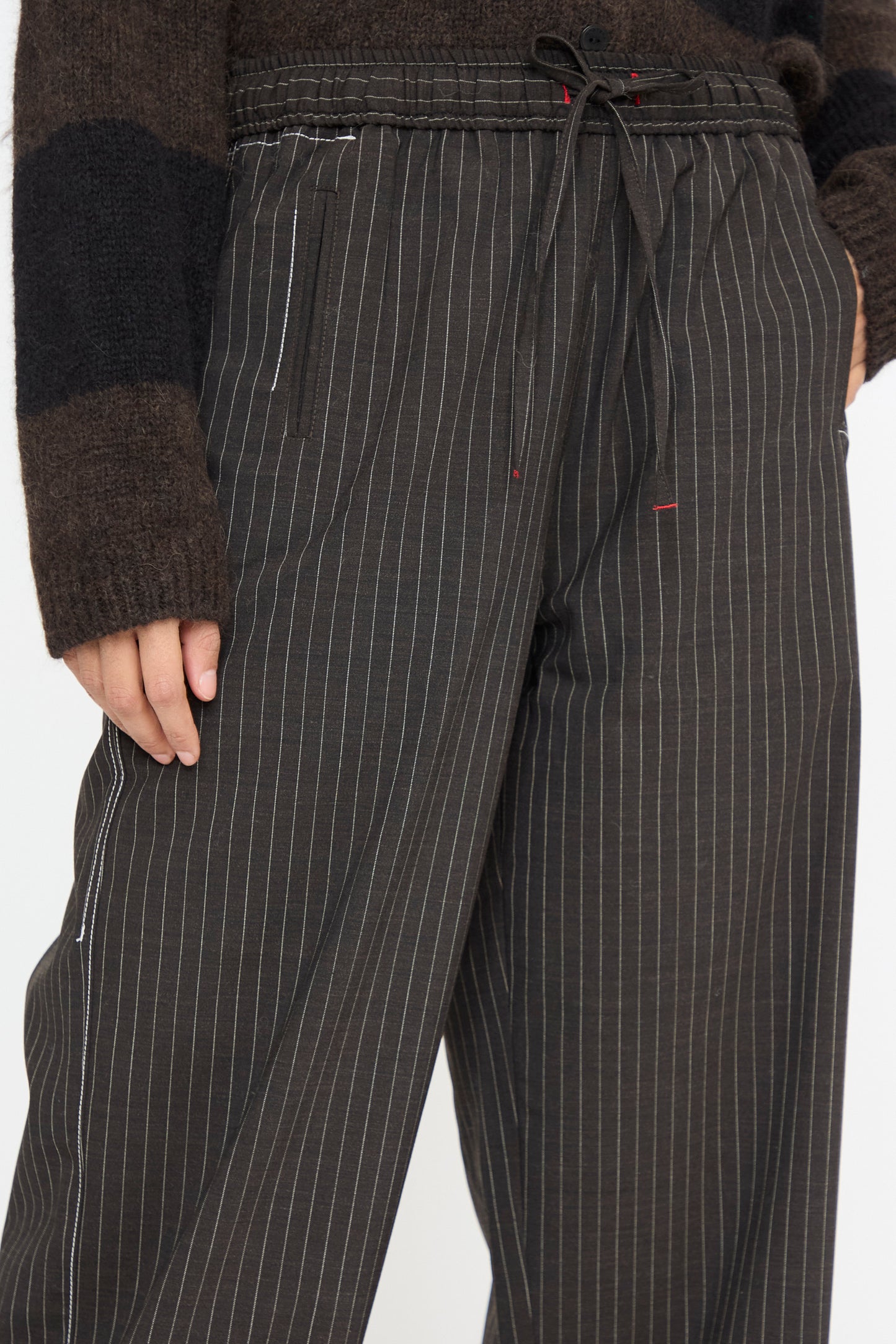 A close up of a person is wearing Cordera's Tailoring Relaxed Pant in Shade, featuring a drawstring waist and made from a refined virgin wool blend, paired with a dark sweater.