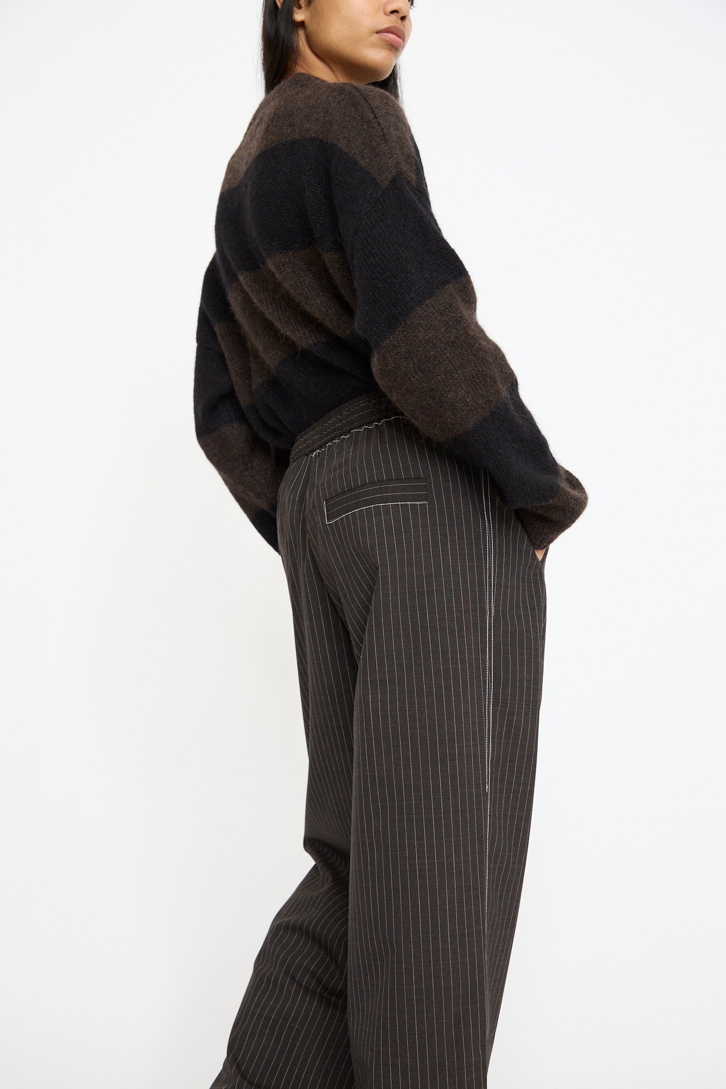 Against a plain white background, a person wears the Cordera Tailoring Relaxed Pant in Shade and a striped sweater. Crafted from a refined virgin wool blend, they pair effortlessly with pinstriped trousers.