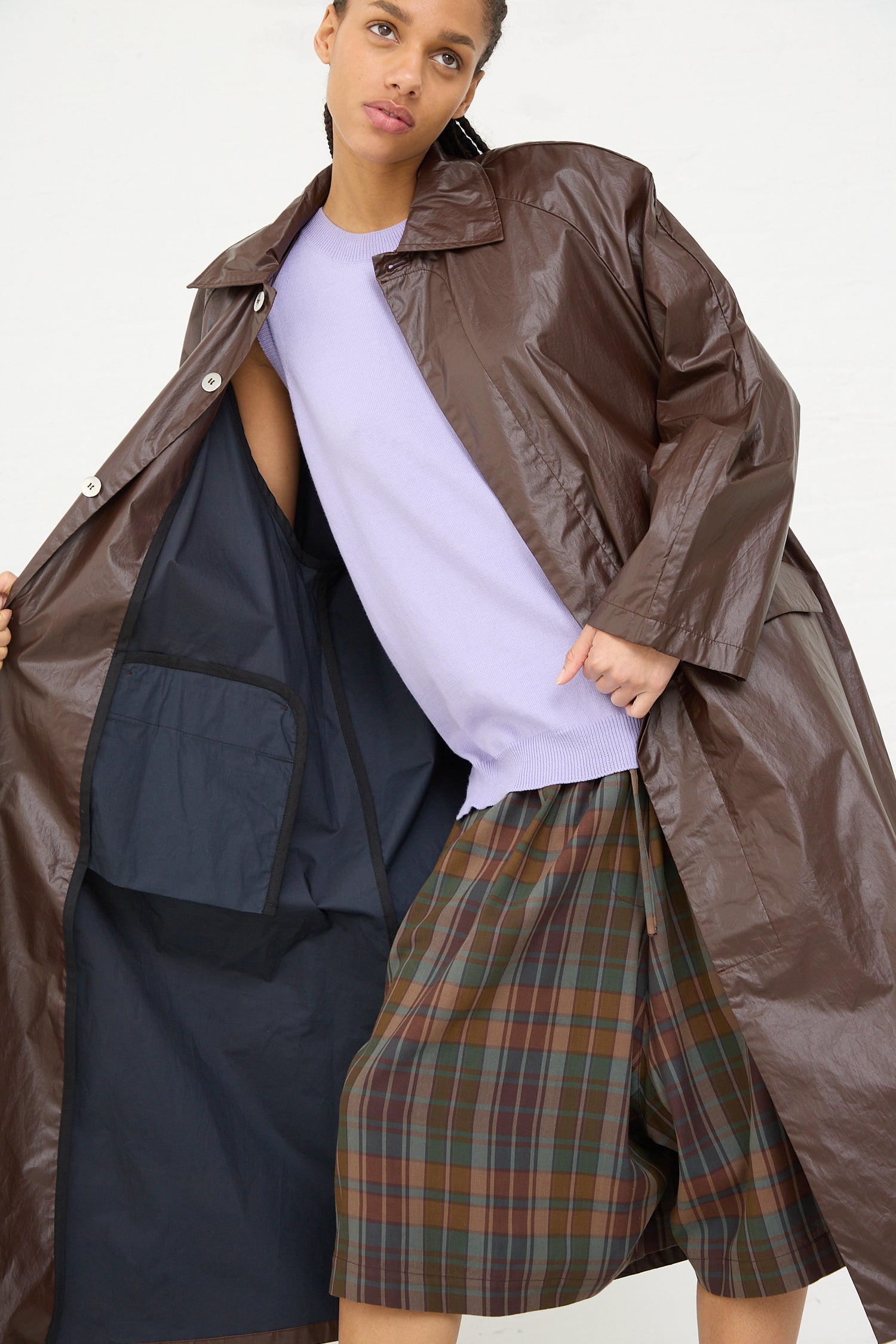 Fashion model showcasing a layered outfit with a purple top, checkered shorts, and an open Cordera Prune Trench Coat.
