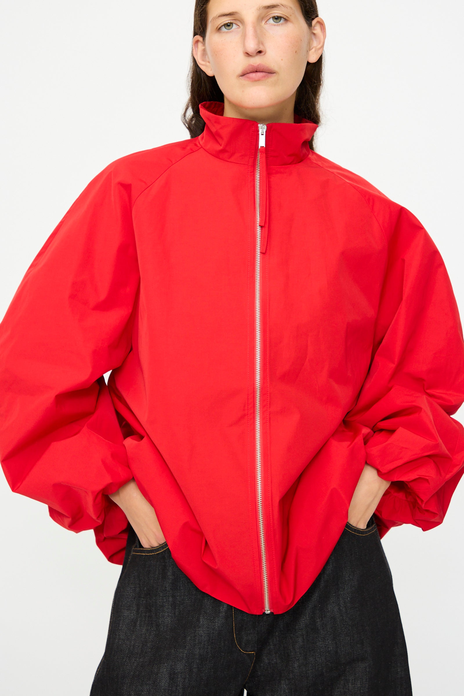 A person wears the Cordera Utility Balloon Jacket in Red, a loose-fitting, water-repellent style with a high collar and wide sleeves, paired with dark pants against a plain white background.