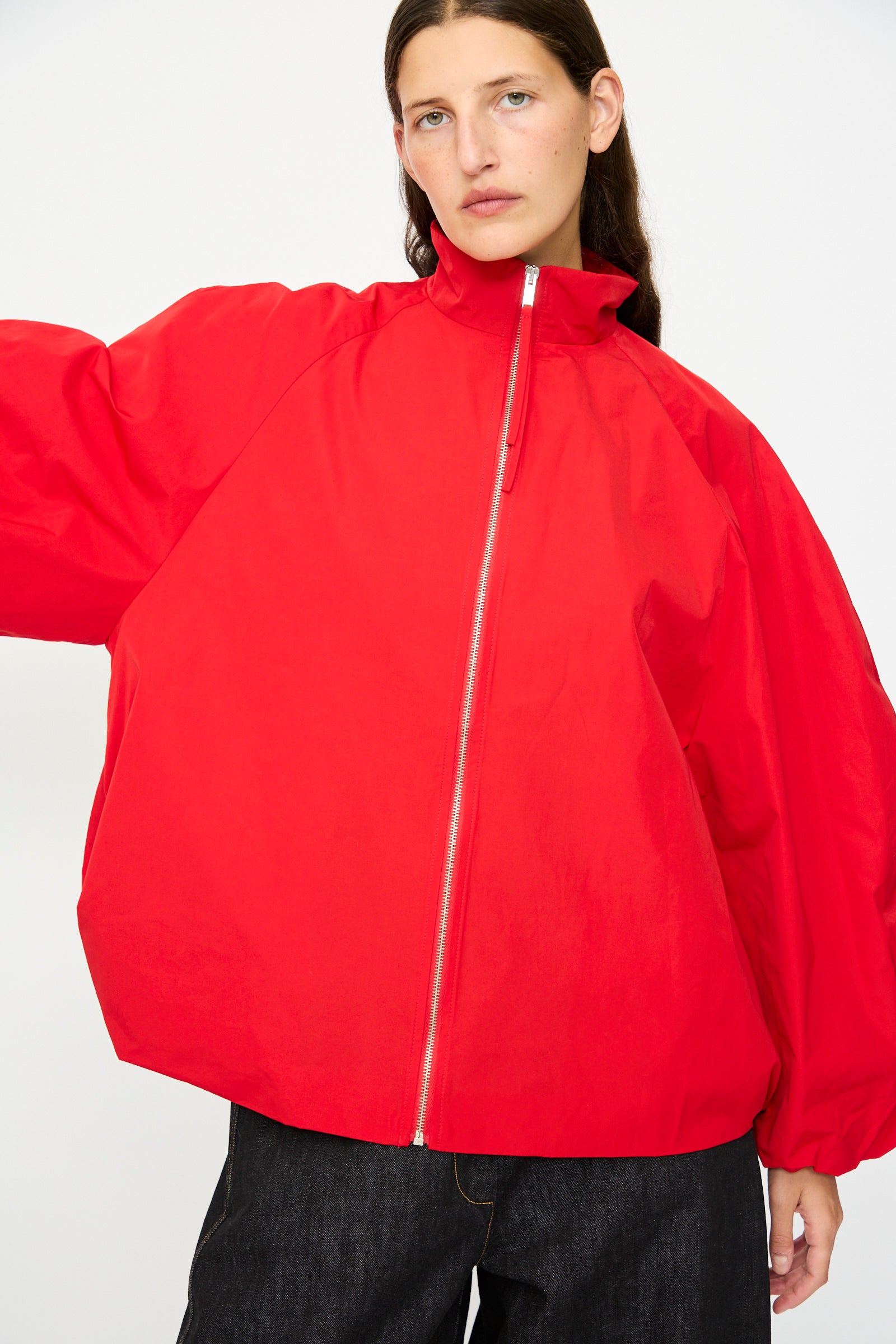 A person wears the Cordera Utility Balloon Jacket in Red—a loose-fitting, water-repellent utility jacket with a high collar—paired with dark pants, standing against a plain white background.