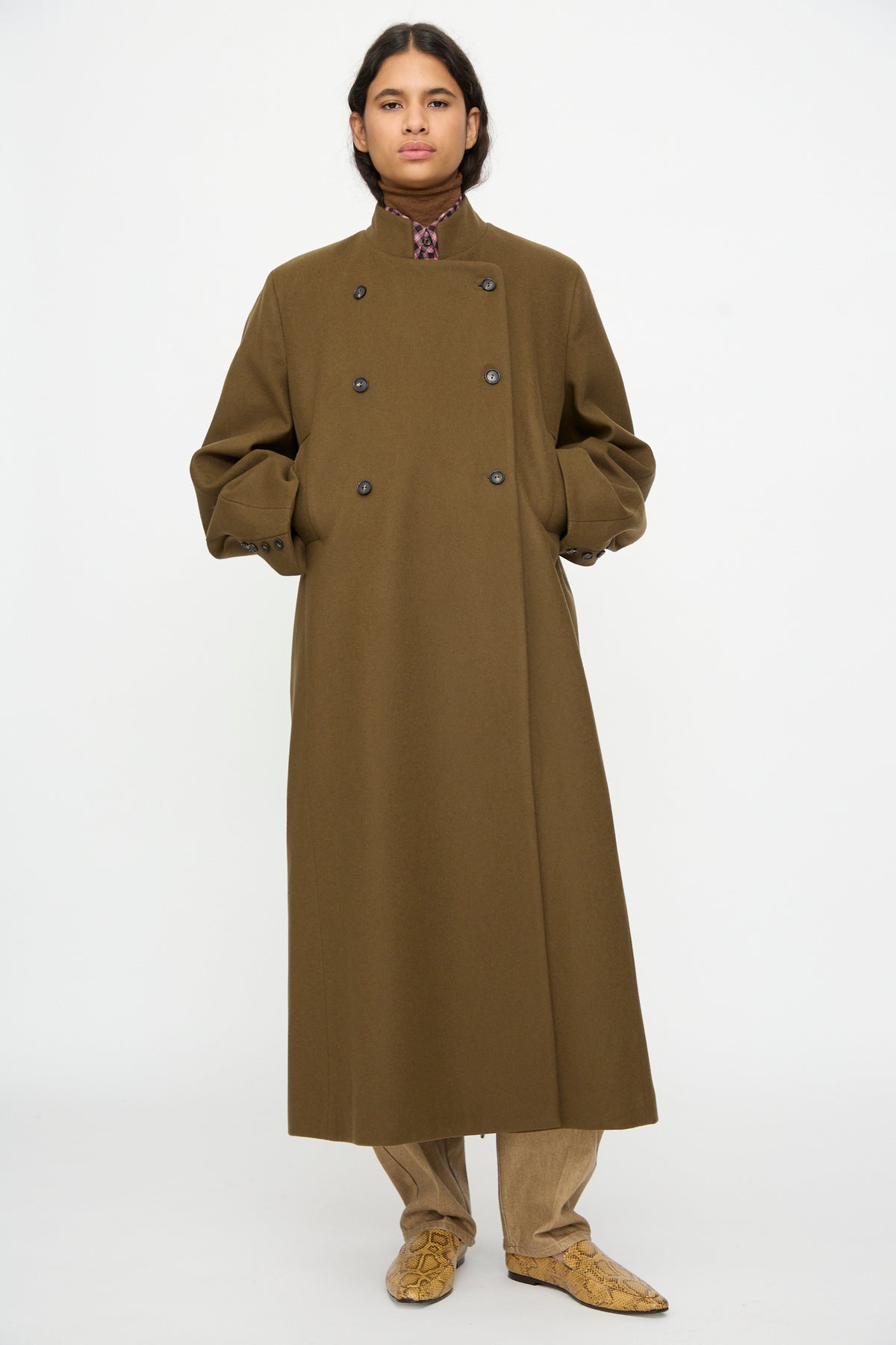 A person wears a Cordera Virgin Wool Long Coat in Pardo over a brown turtleneck and light brown trousers, finished with snakeskin-print pointed-toe shoes.