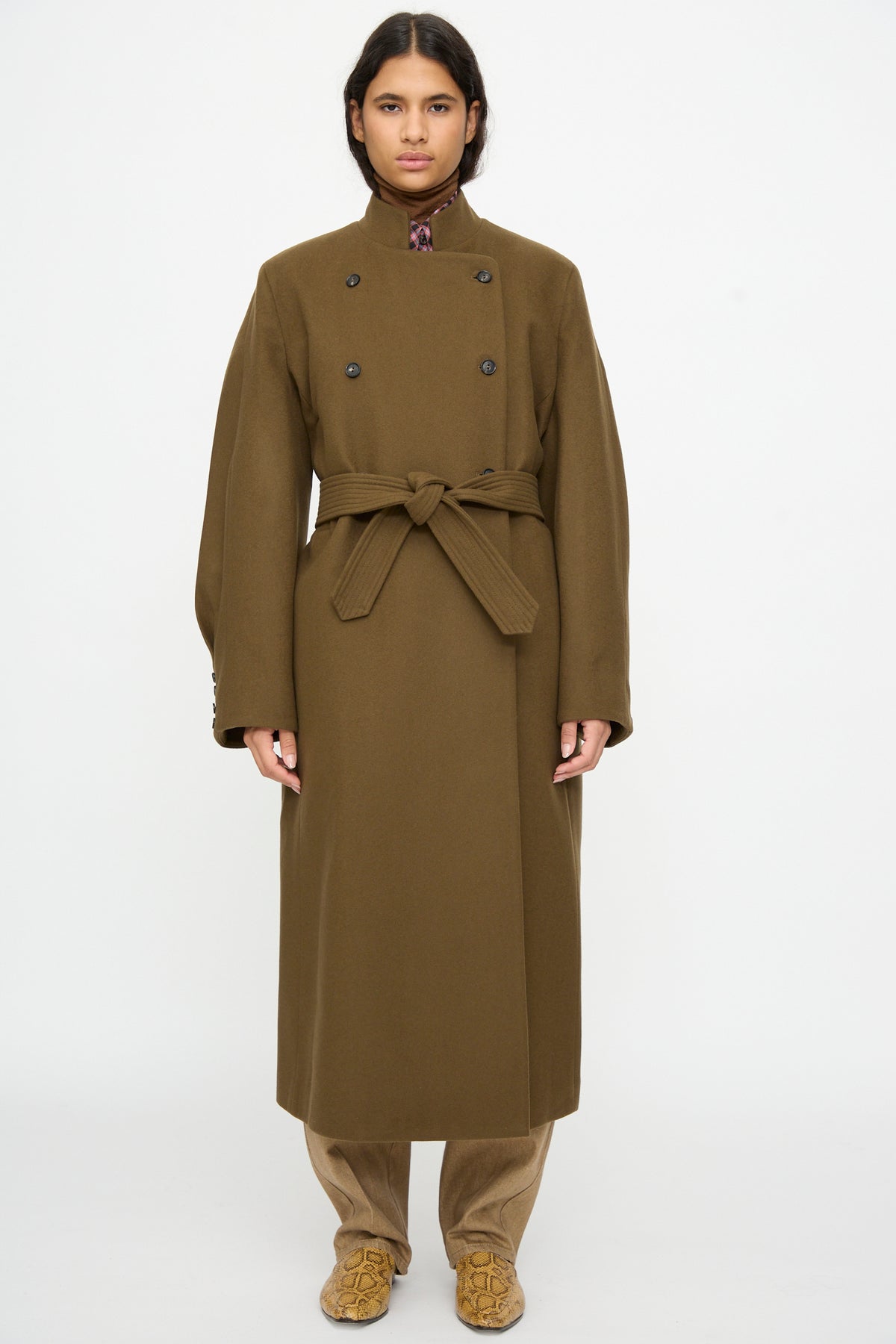 A person wearing an olive green, double-breasted, oversized Virgin Wool Long Coat in Pardo by Cordera, featuring a matching tie belt at the waist.