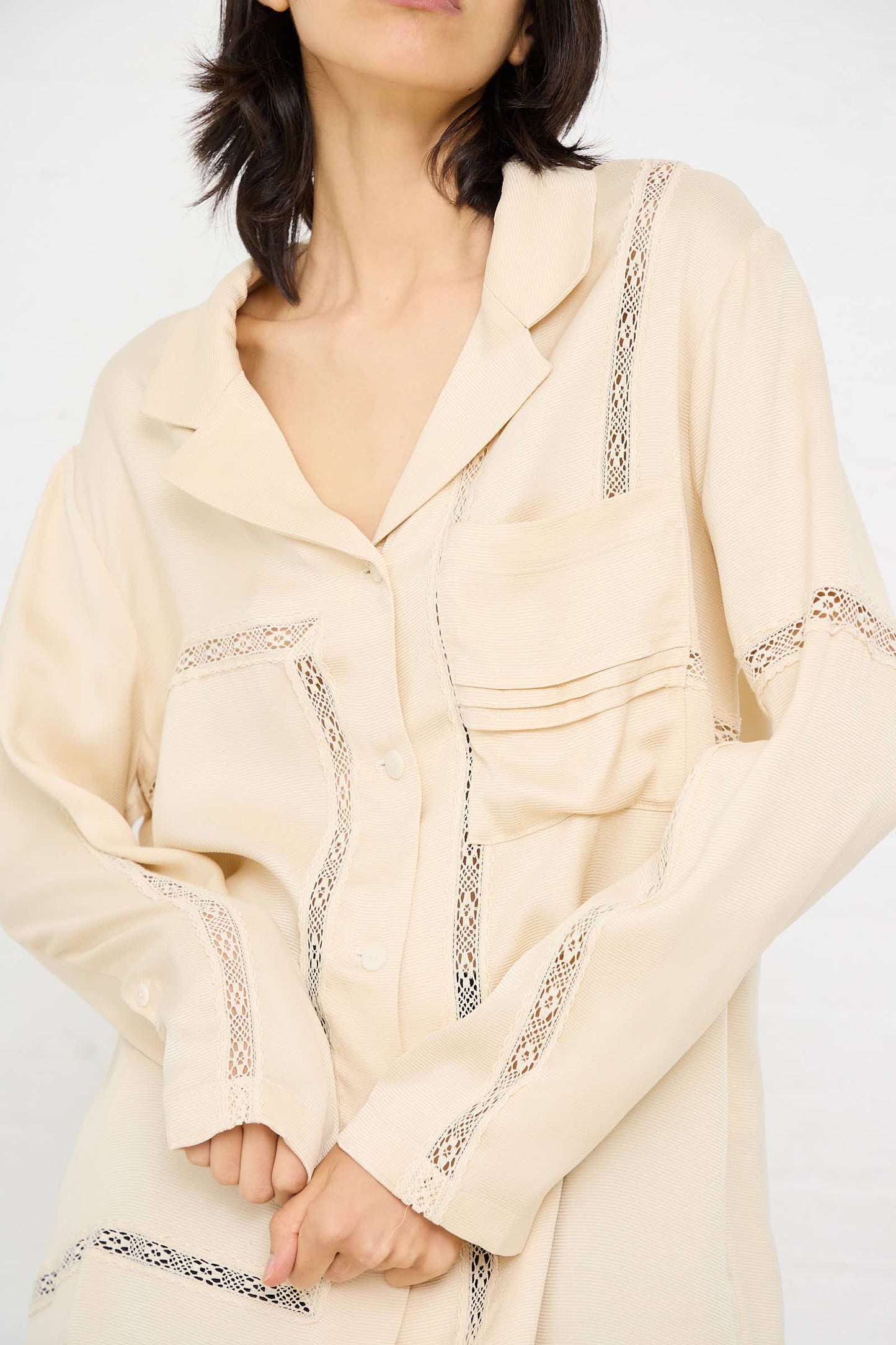 A person wearing the Cordera Viscose Shirt with Lace in Shell stands against a plain background. The beige oversized fit shirt features a relaxed silhouette with lace trim details, a folded collar, and a button-down front.