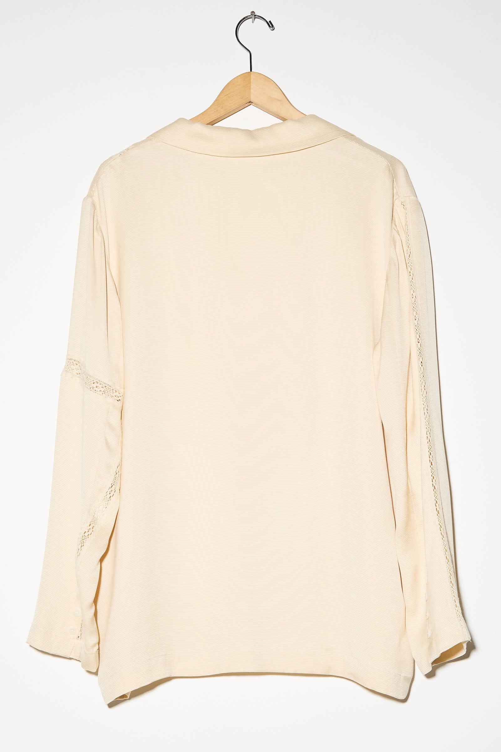 The Shell Viscose Shirt with Lace by Cordera, featuring an oversized fit and elegant viscose lace details on the sleeves, hangs on a wooden hanger against a white background.