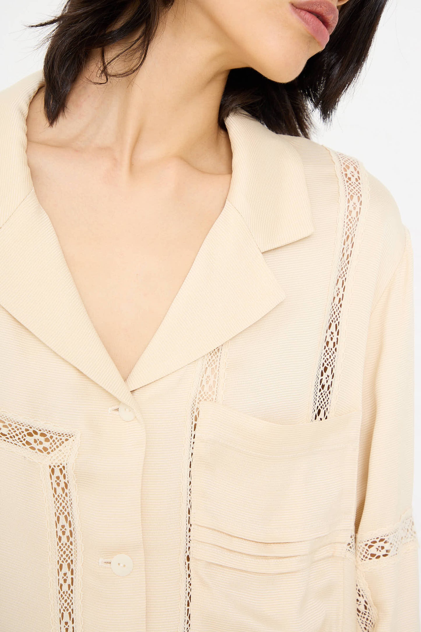 A person wearing the Cordera Viscose Shirt with Lace in Shell, featuring an oversized fit and lace detailing near the collar and pockets. The person's face is partially visible.