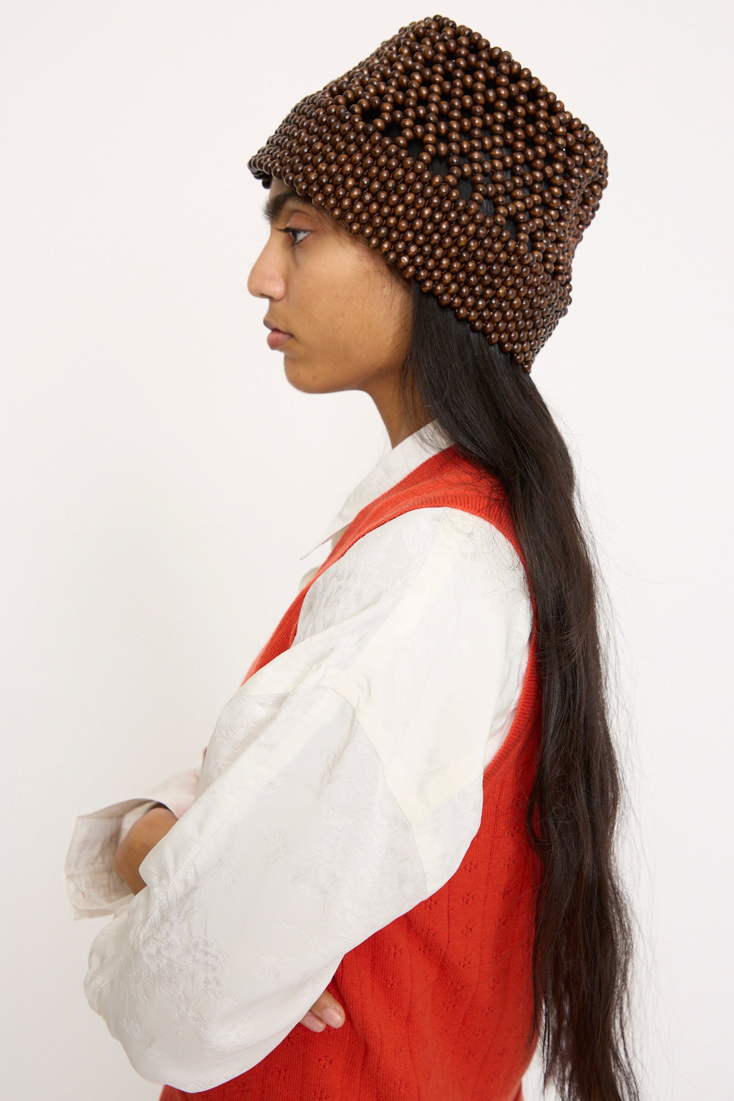 Person in profile wearing a white shirt, red vest, and Cordera's Wooden Beads Bucket Hat in Brown with long dark hair.