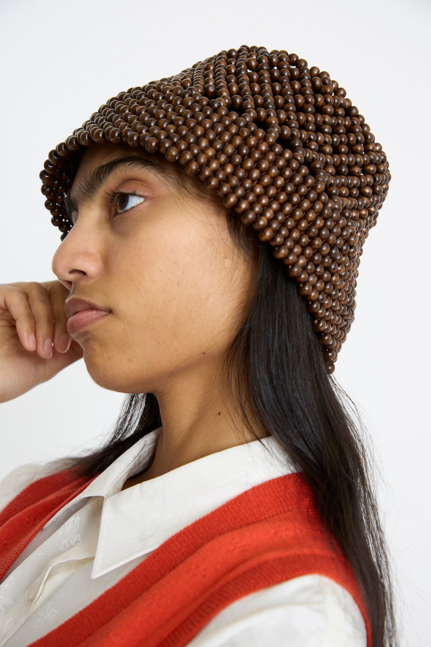 A person in a red vest and white shirt wears Cordera's Wooden Beads Bucket Hat in Brown, gazing sideways against a plain background.