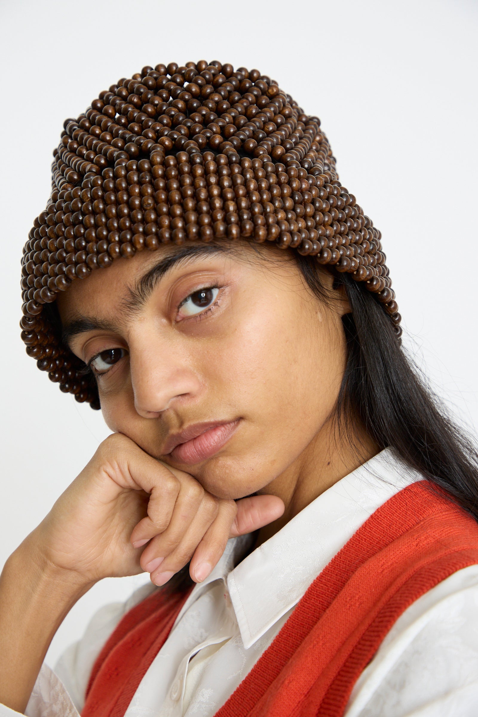 Person wearing a Cordera Wooden Beads Bucket Hat in Brown with an orange and white top, resting their chin on their hand, gazing directly at the camera against a plain white background.