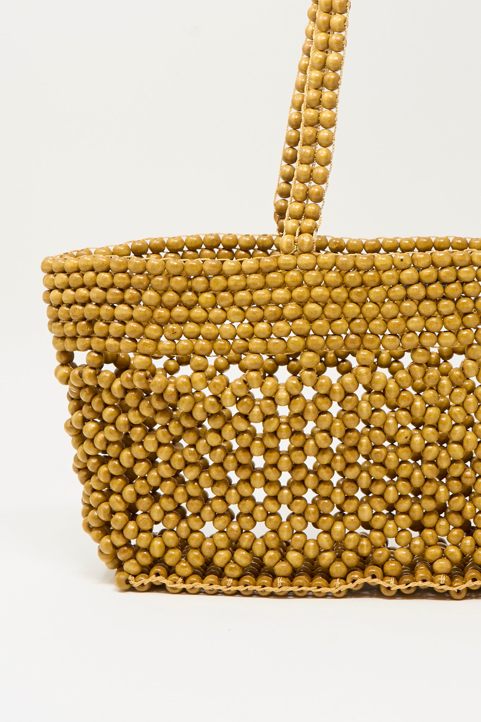 A close-up of Cordera's Wooden Beads Mini Bag in Ochre, handcrafted from round yellow beads with a matching beaded handle, set against a plain white background.