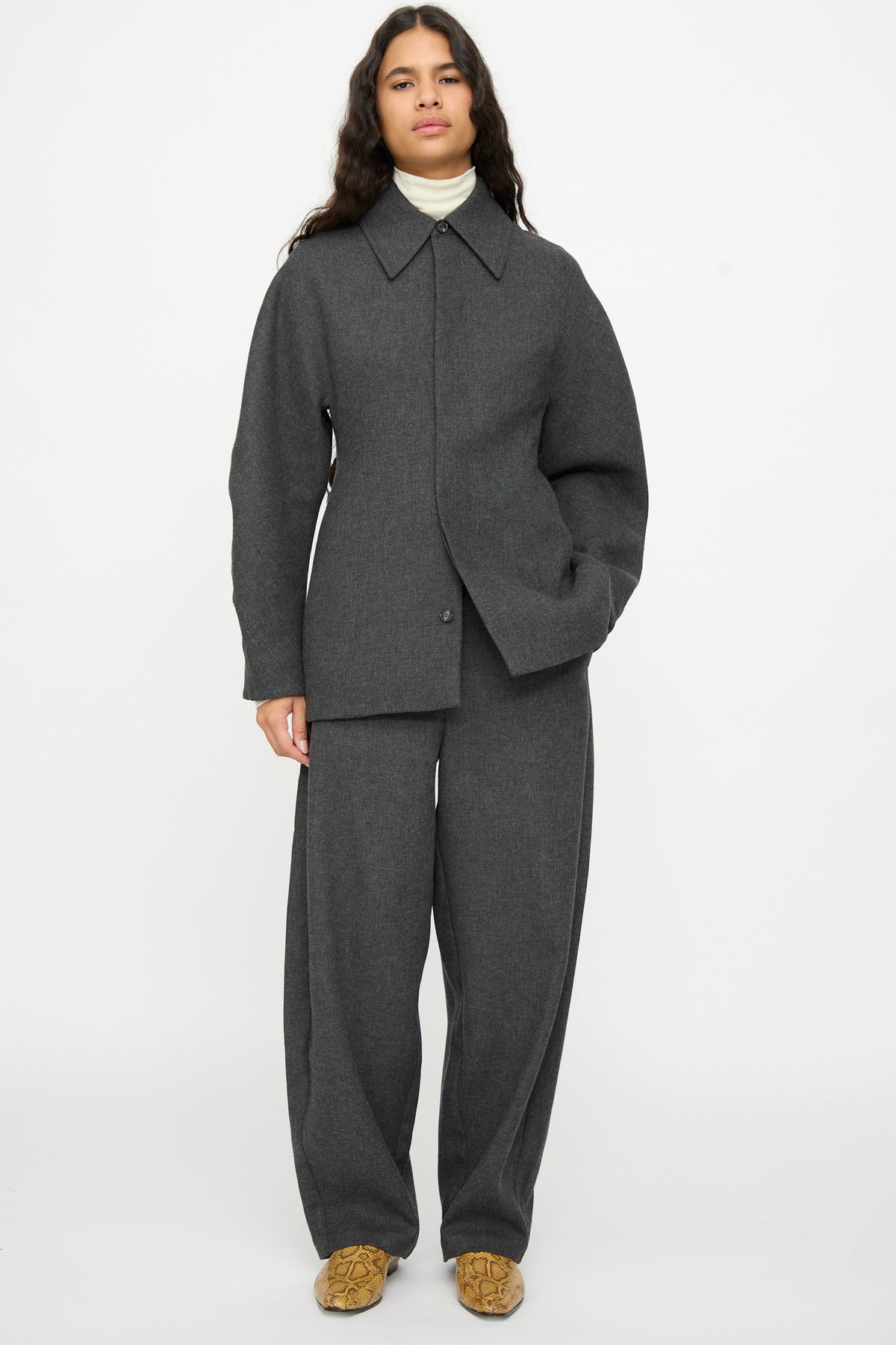 A person wearing a charcoal gray wool jacket and matching Cordera Wool Curved Pants in Anthracite over a cream turtleneck.